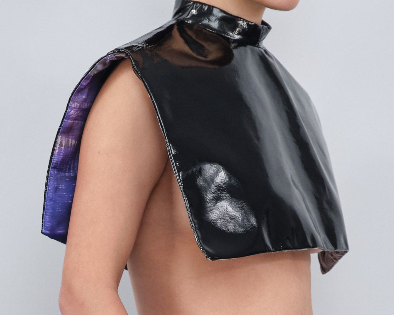 A woman without a shirt is wearing a black cape