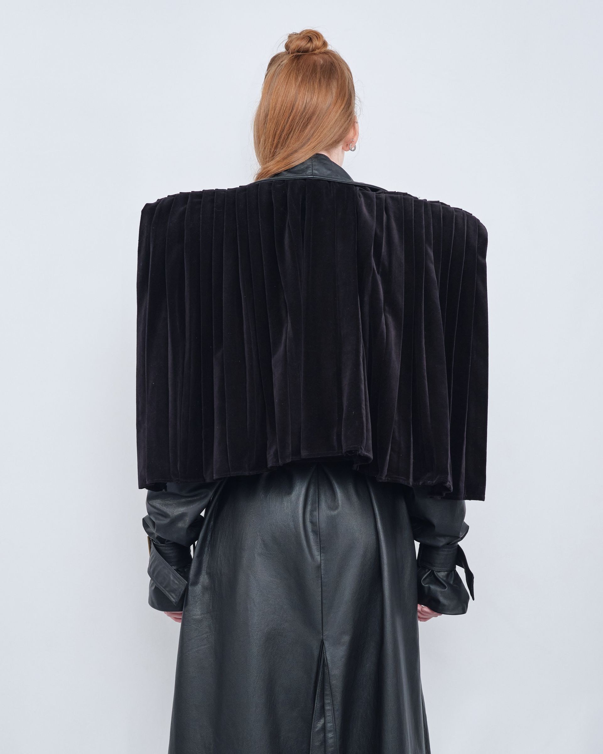 A woman is wearing a black coat with a square shaped shoulder.