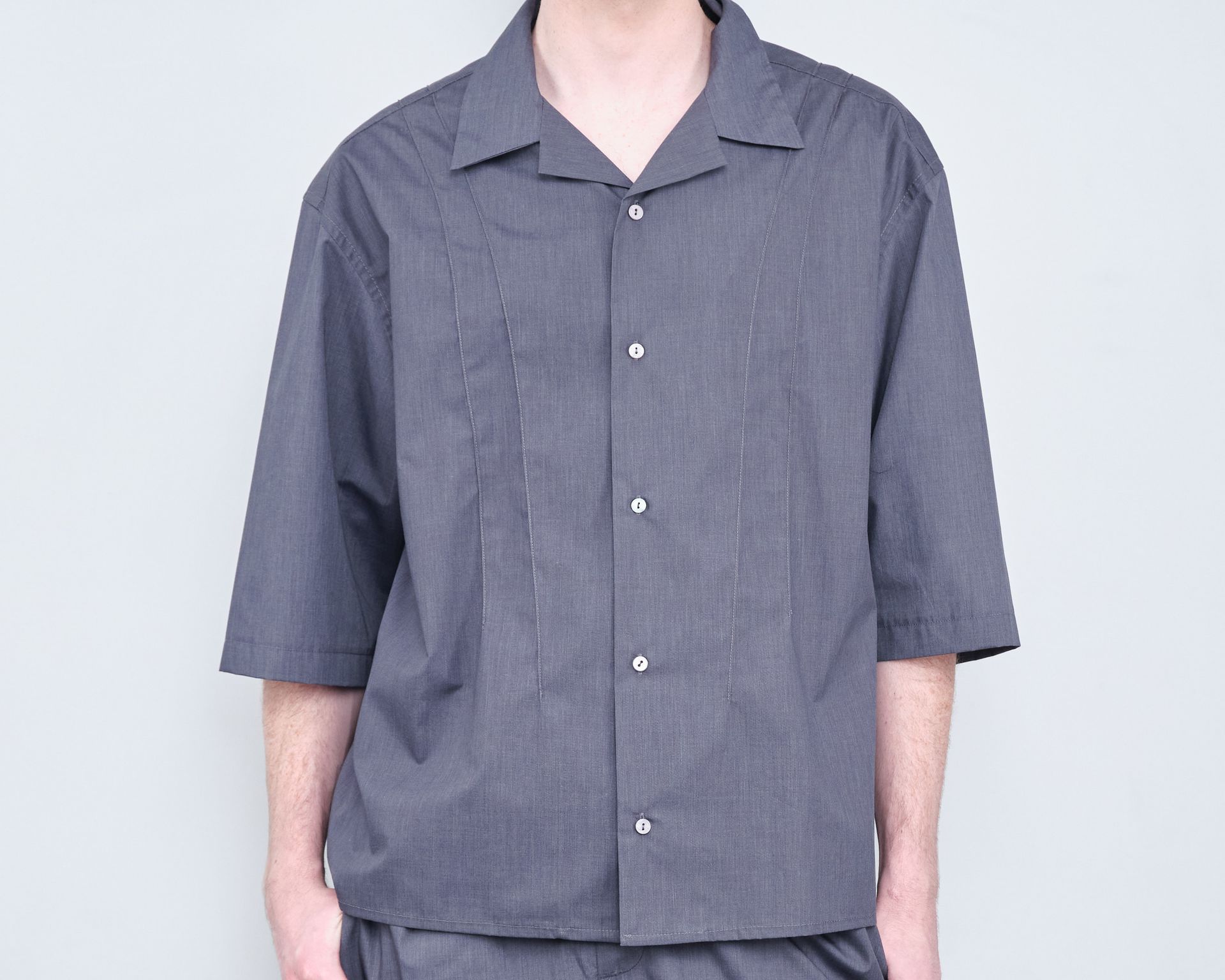 A man wearing a grey shirt and shorts is standing in front of a white wall.