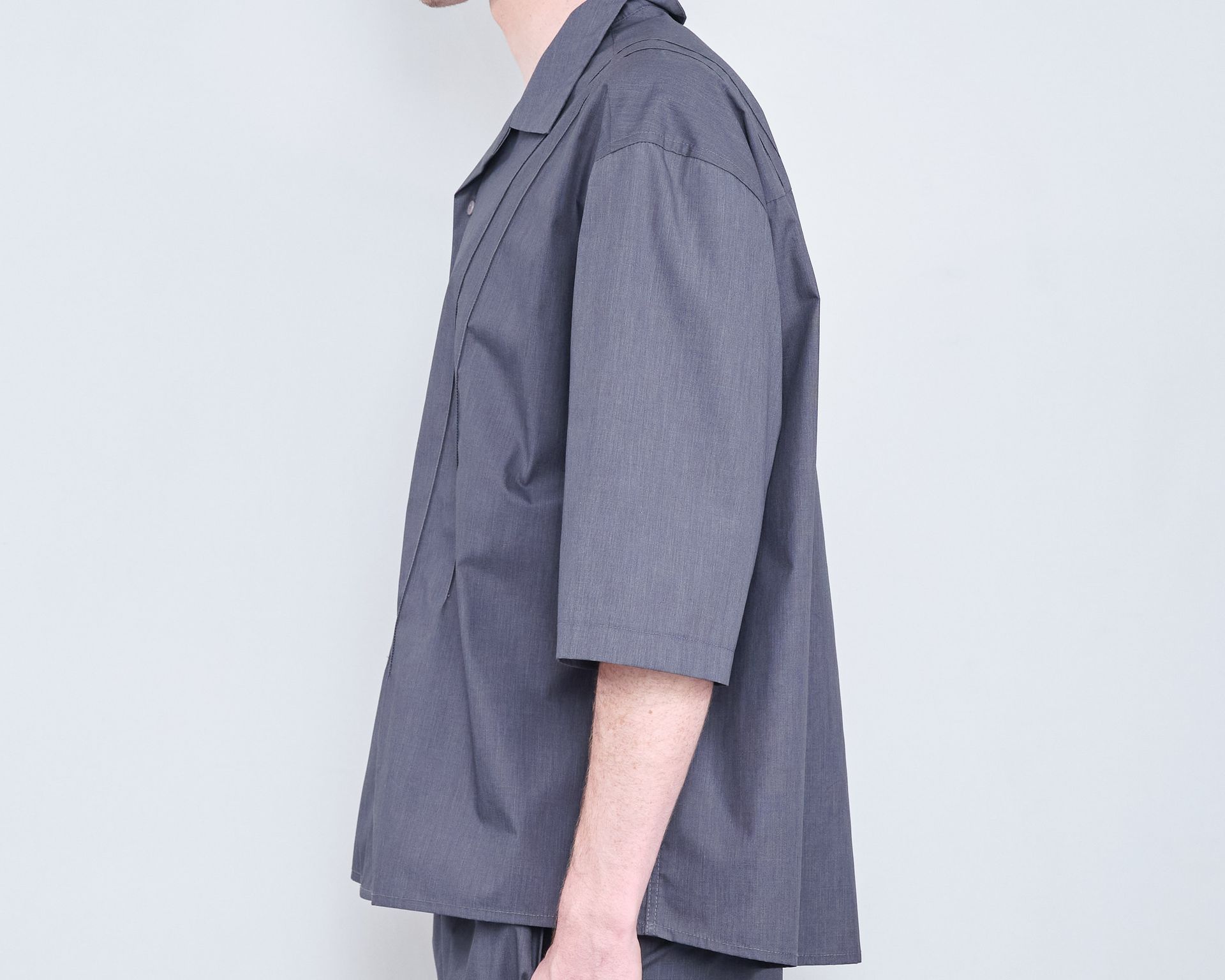 A man wearing a gray shirt and pants is standing in front of a white wall.