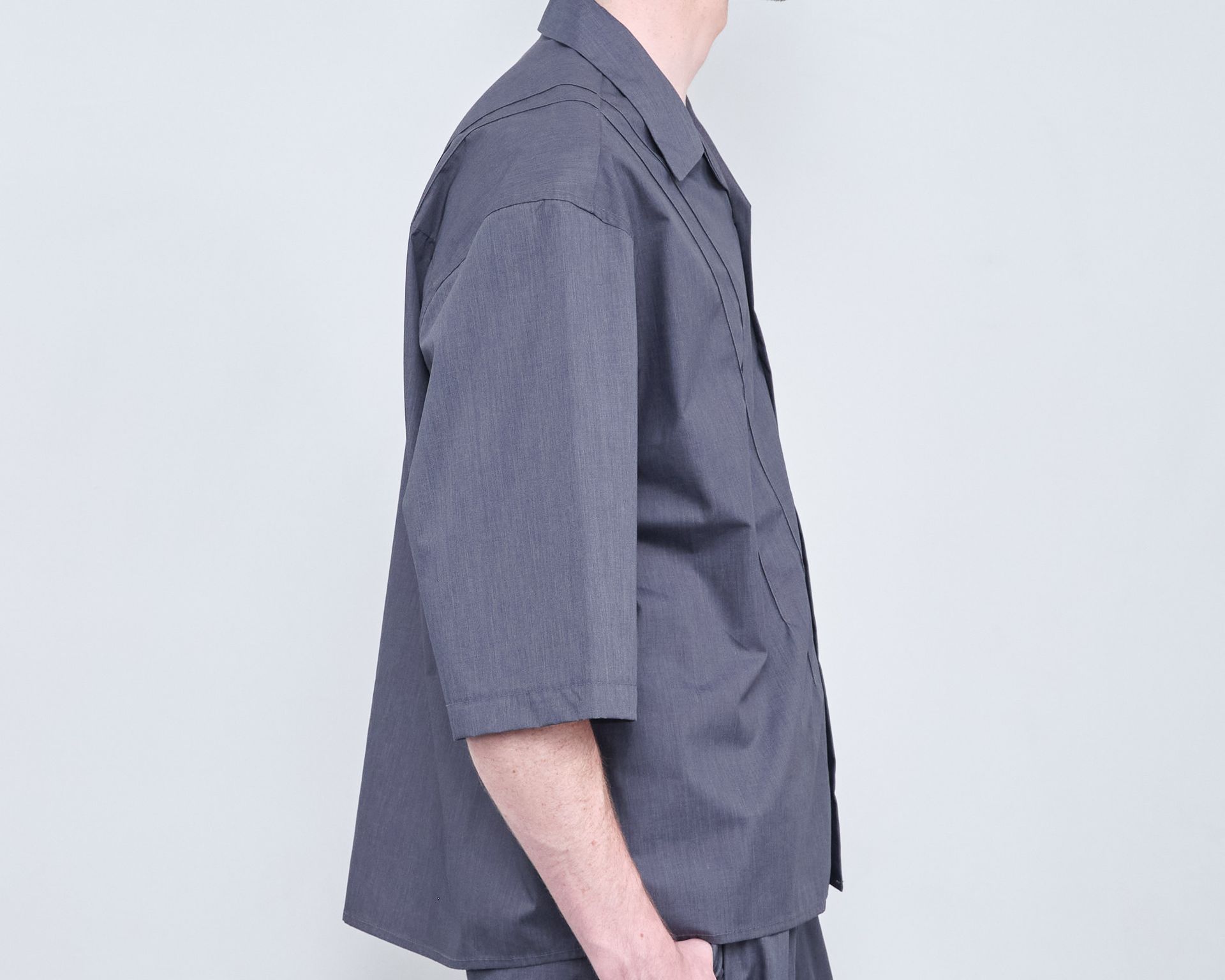 A man wearing a grey shirt and shorts is standing in front of a white wall.