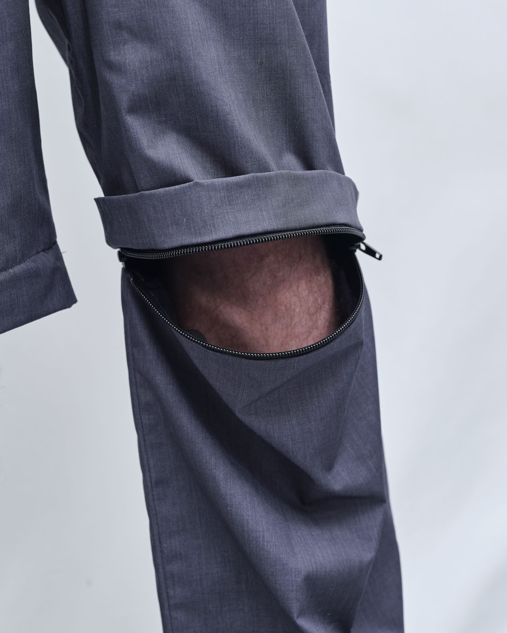 A man wearing a gray shirt and pants is standing with his hands in his pockets.