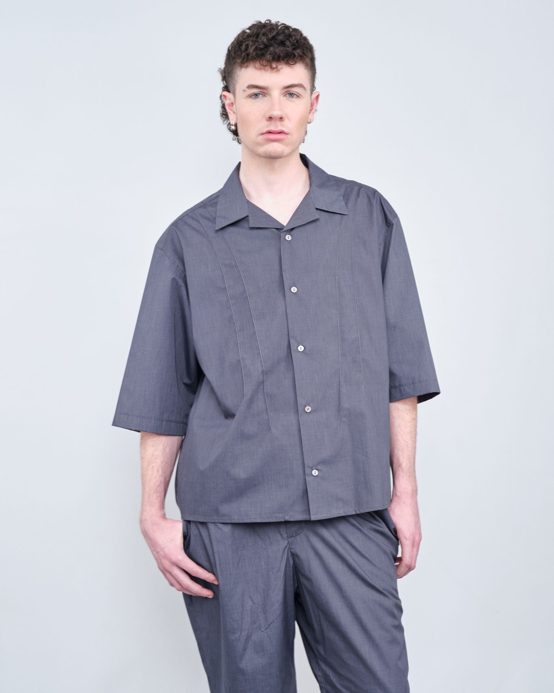 A man wearing a gray shirt and pants is standing with his hands in his pockets.