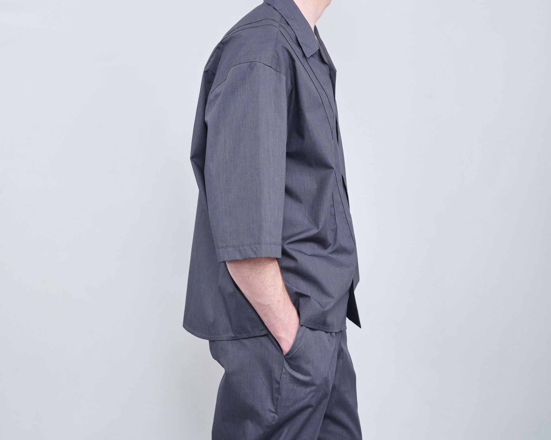 A man wearing a gray shirt and pants is standing with his hands in his pockets.