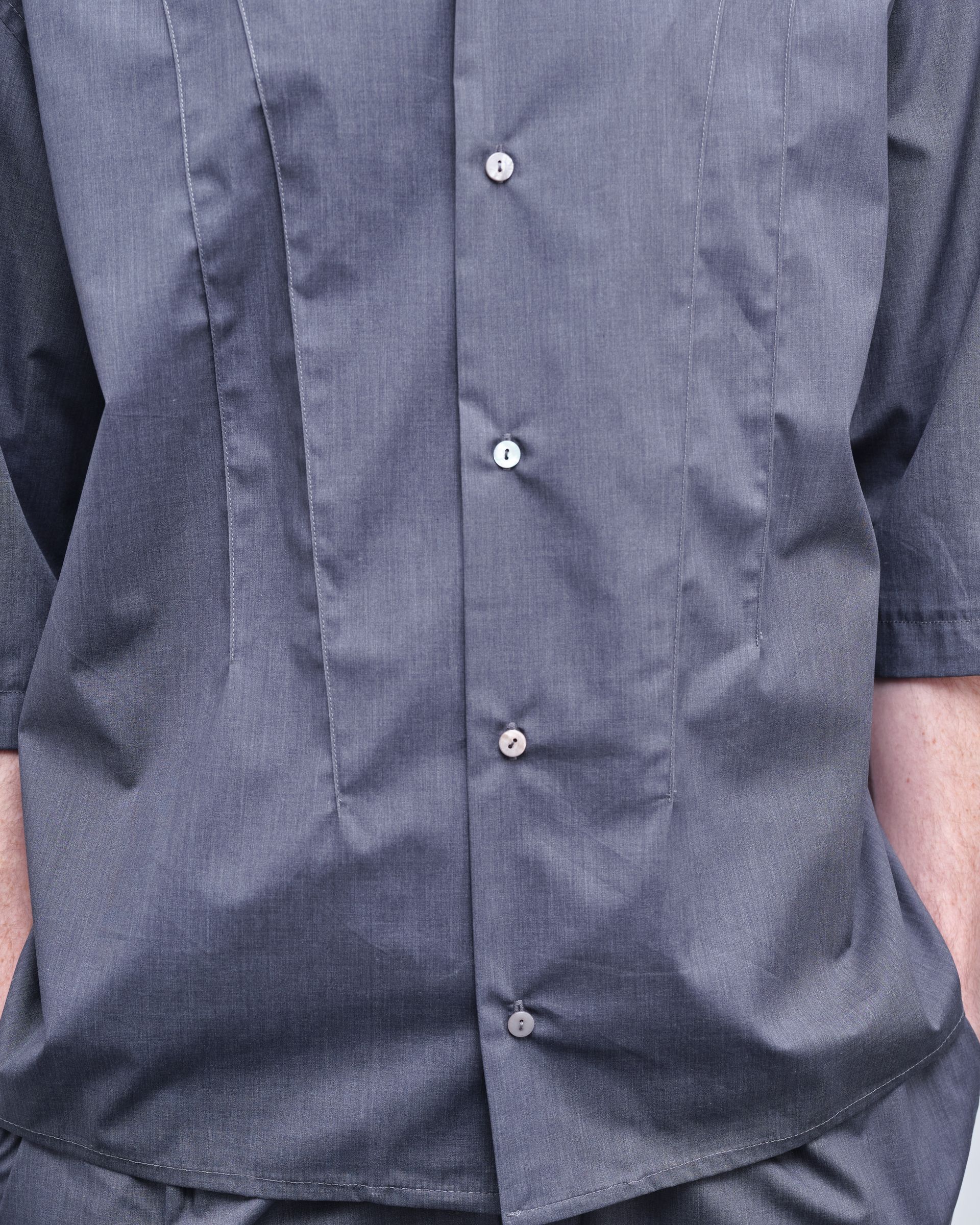 A close up of a person wearing a grey shirt with buttons