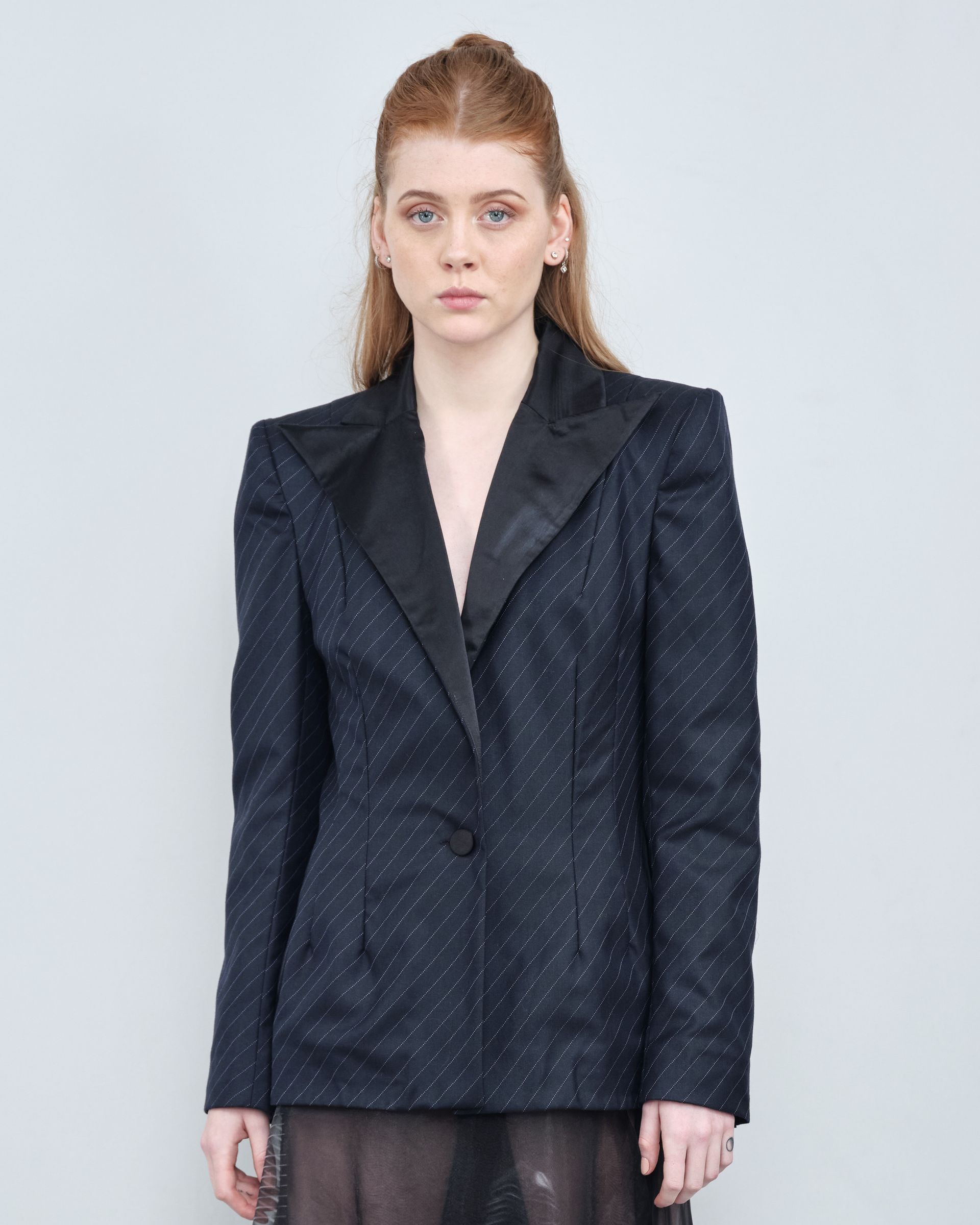 A woman is wearing a black tuxedo jacket and a black dress.