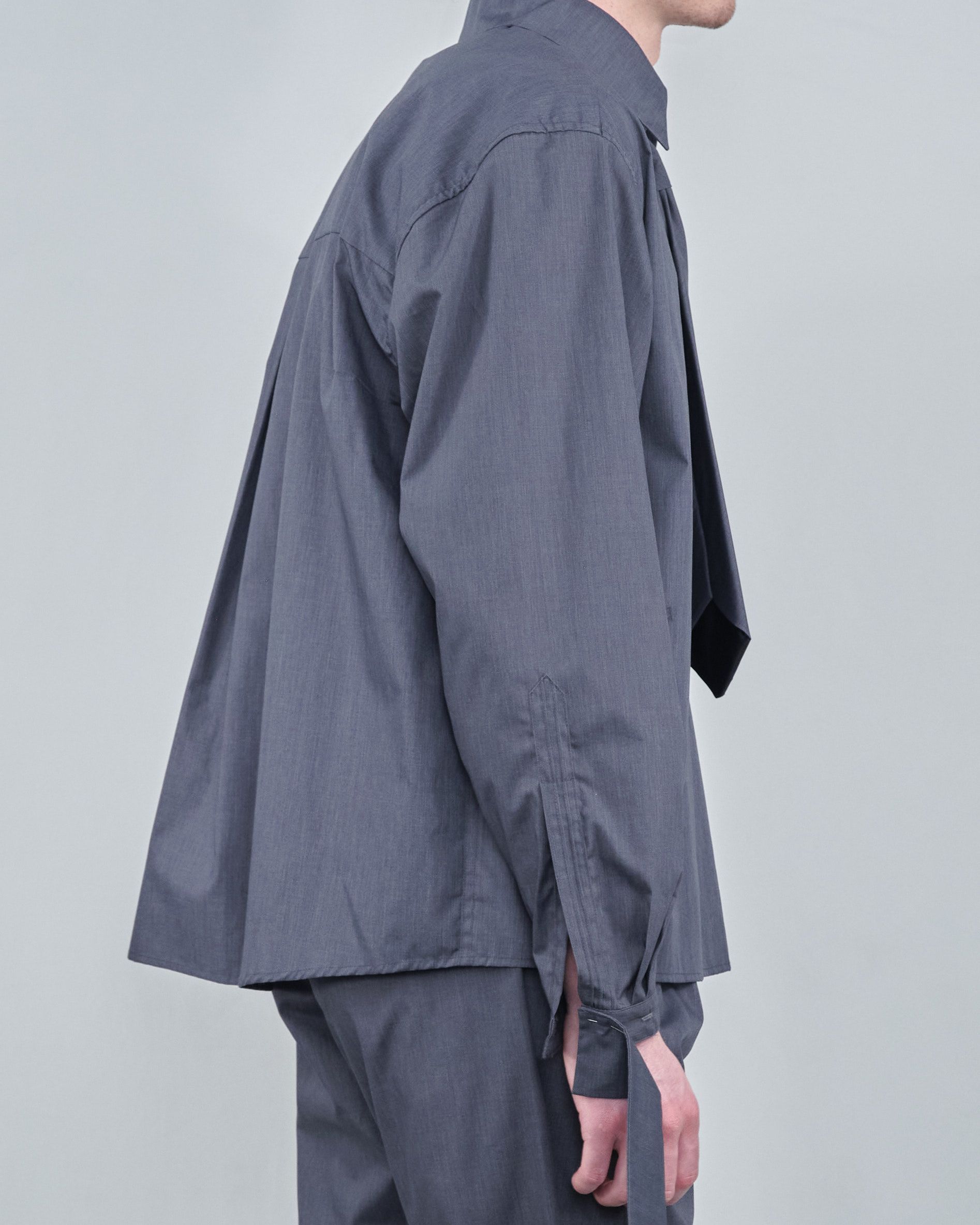 A man wearing a gray shirt and pants is standing in front of a white wall.