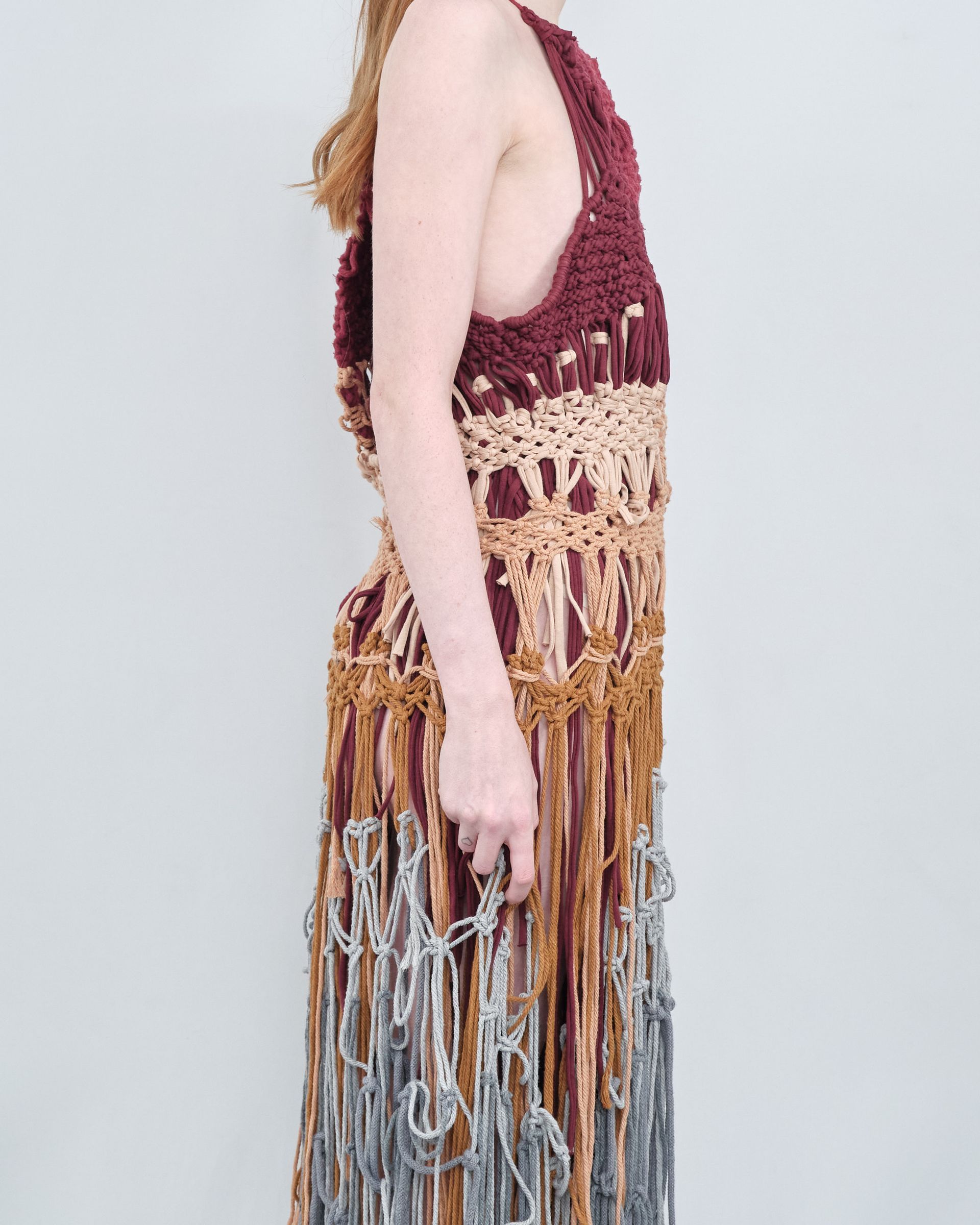 A woman is wearing a crocheted dress with fringe.