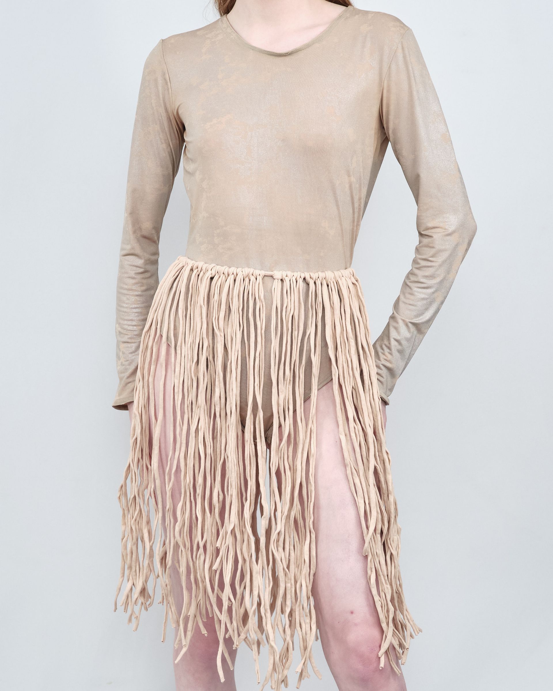 A woman is wearing a tan dress with fringe on the skirt