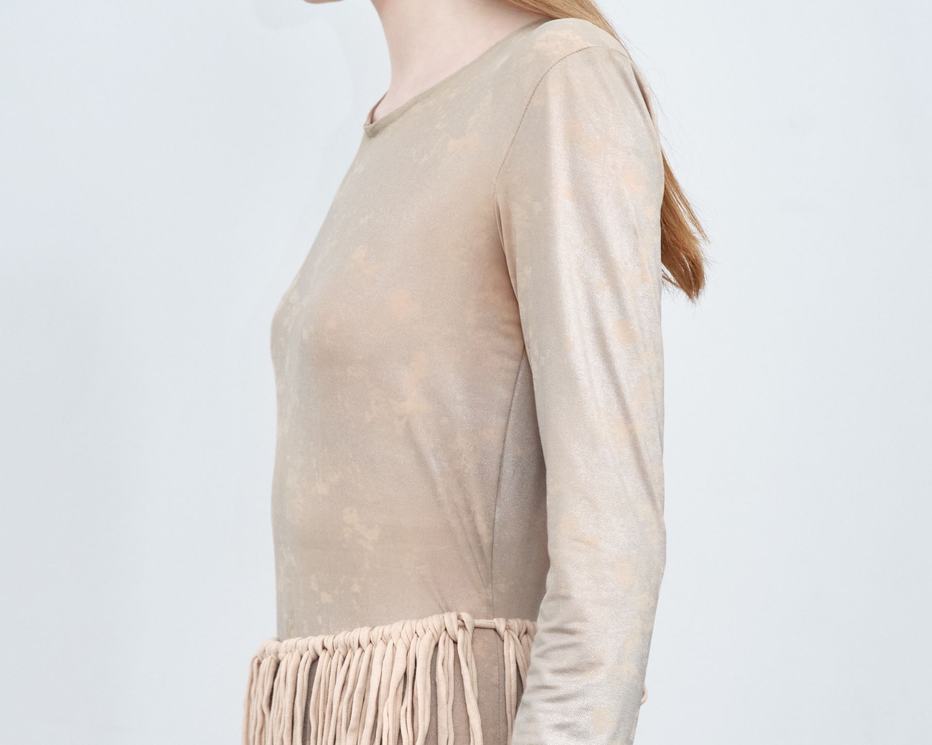 A woman is wearing a tan dress with fringe on the sleeves