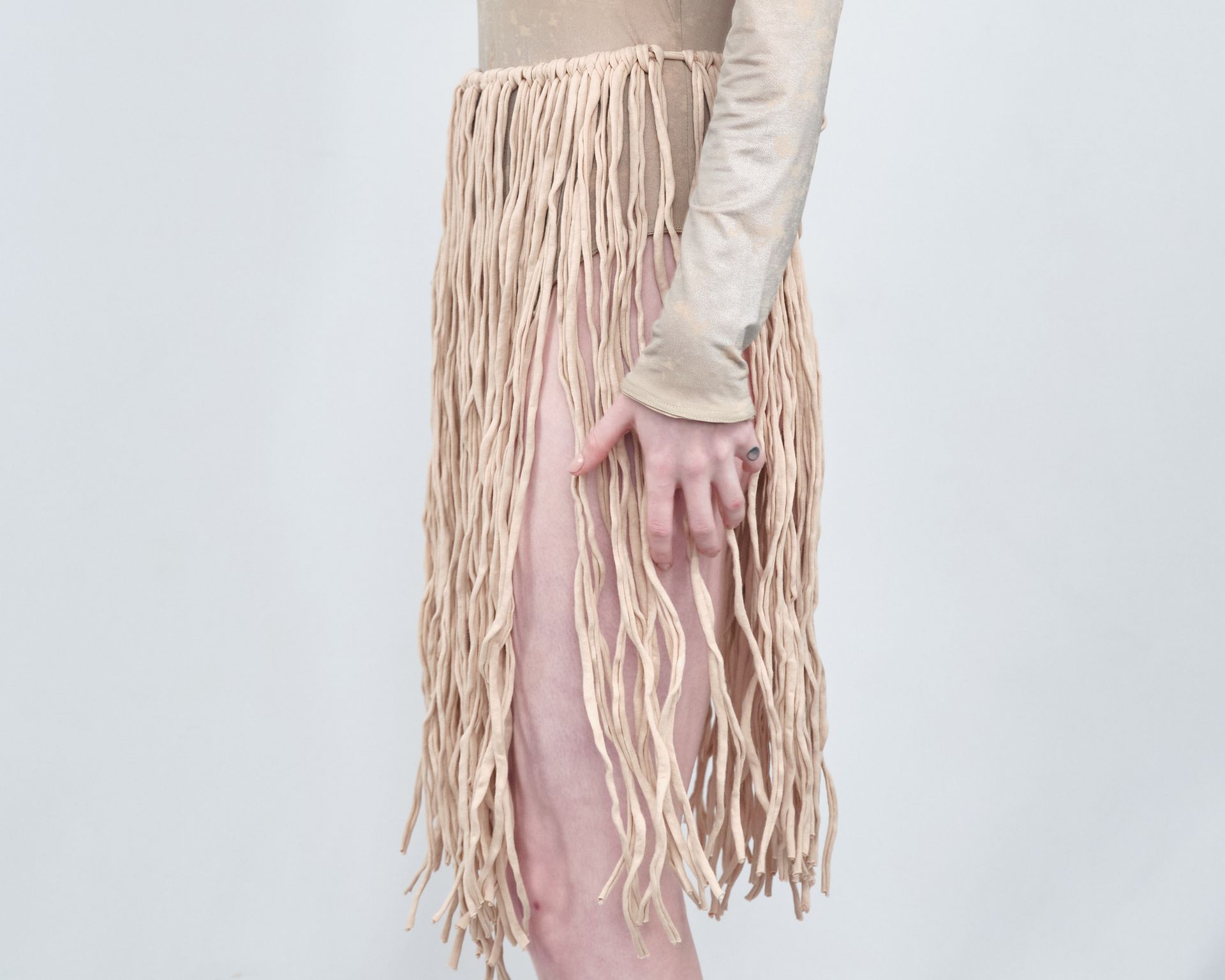 A woman is wearing a skirt with fringe and a ring on her finger.