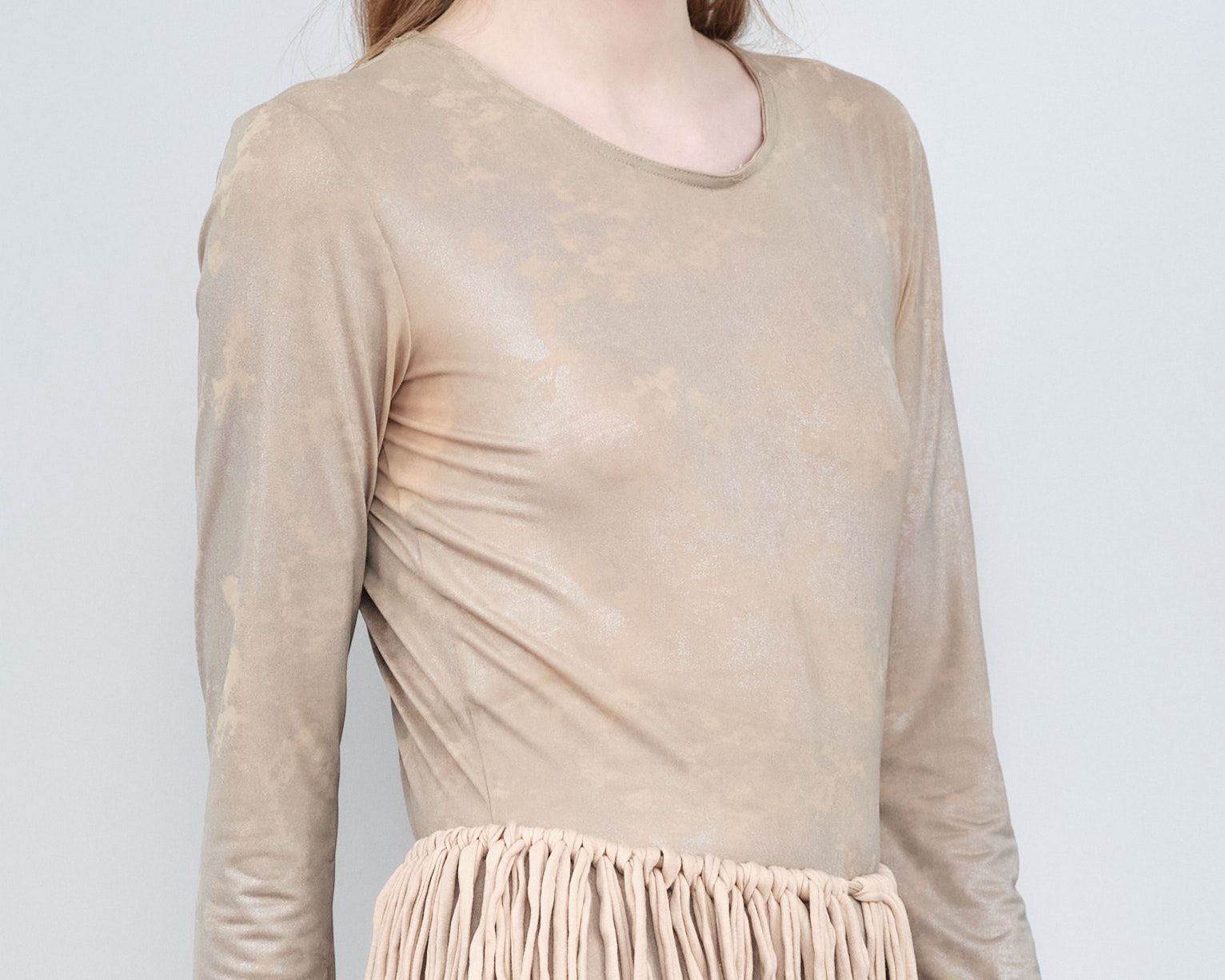 A woman is wearing a long sleeve tan shirt and a skirt with fringe.