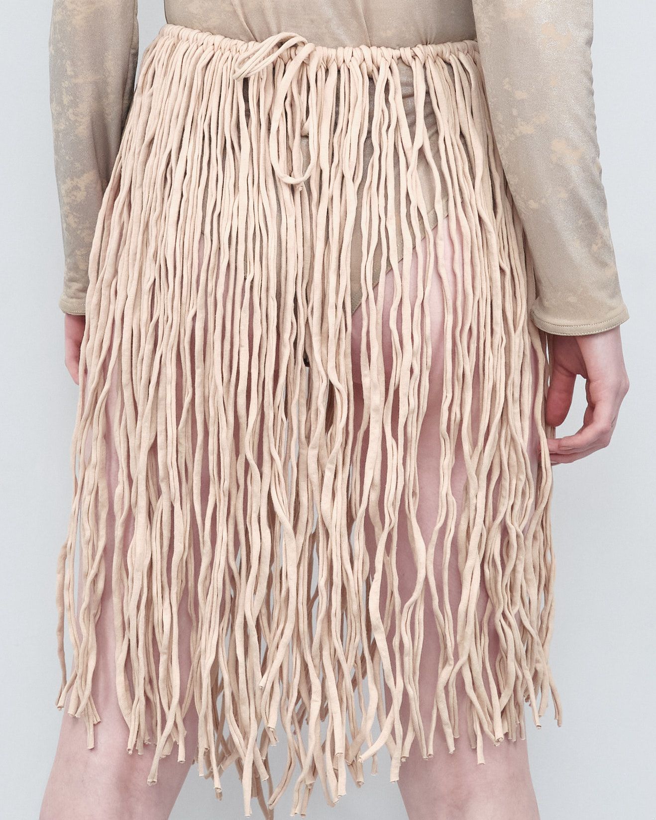 A woman is wearing a tan fringed skirt