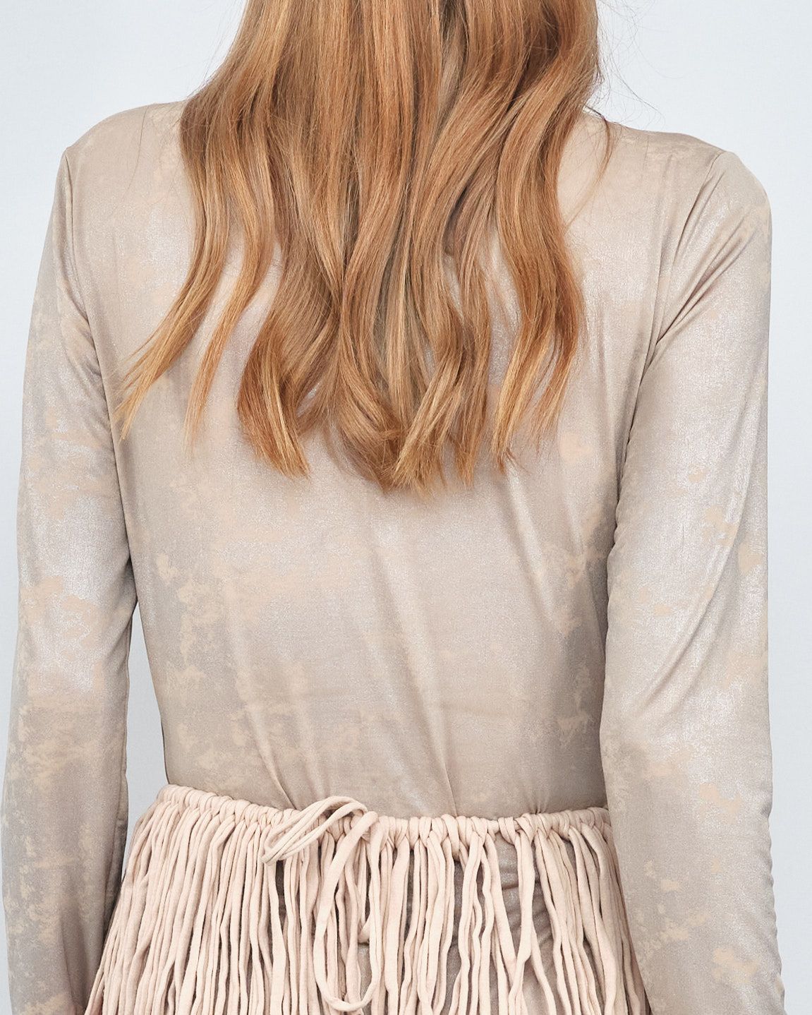 The back of a woman wearing a long sleeve top and a skirt with fringe.