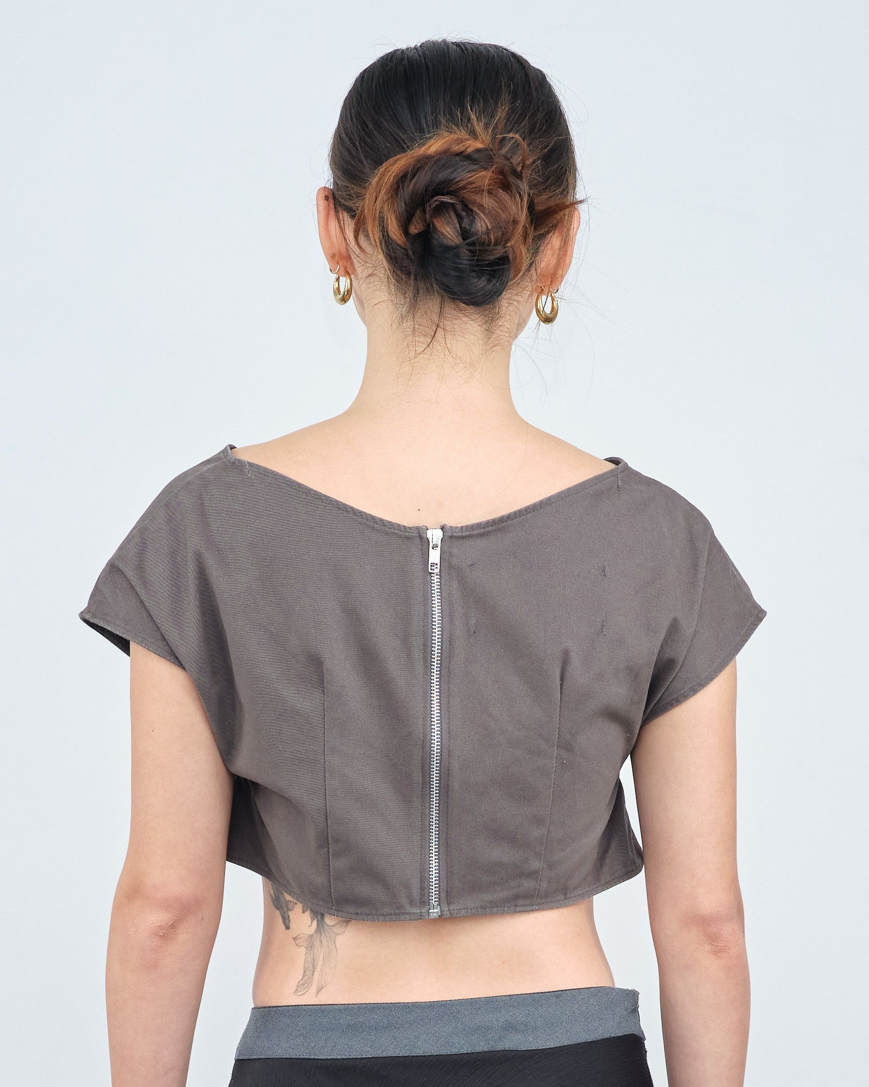 The back of a woman wearing a crop top and earrings.