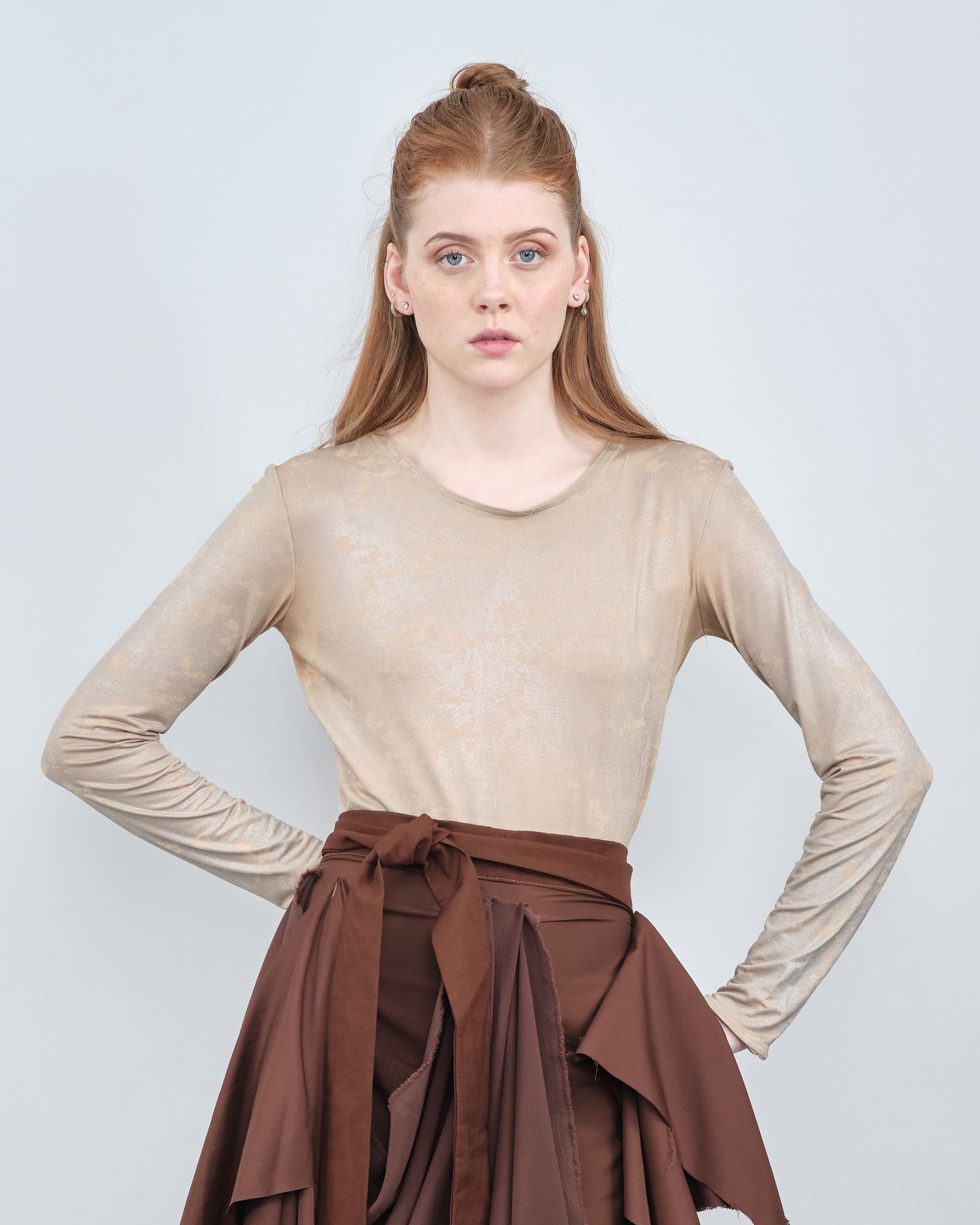 A woman is wearing a long sleeve top and a brown skirt.