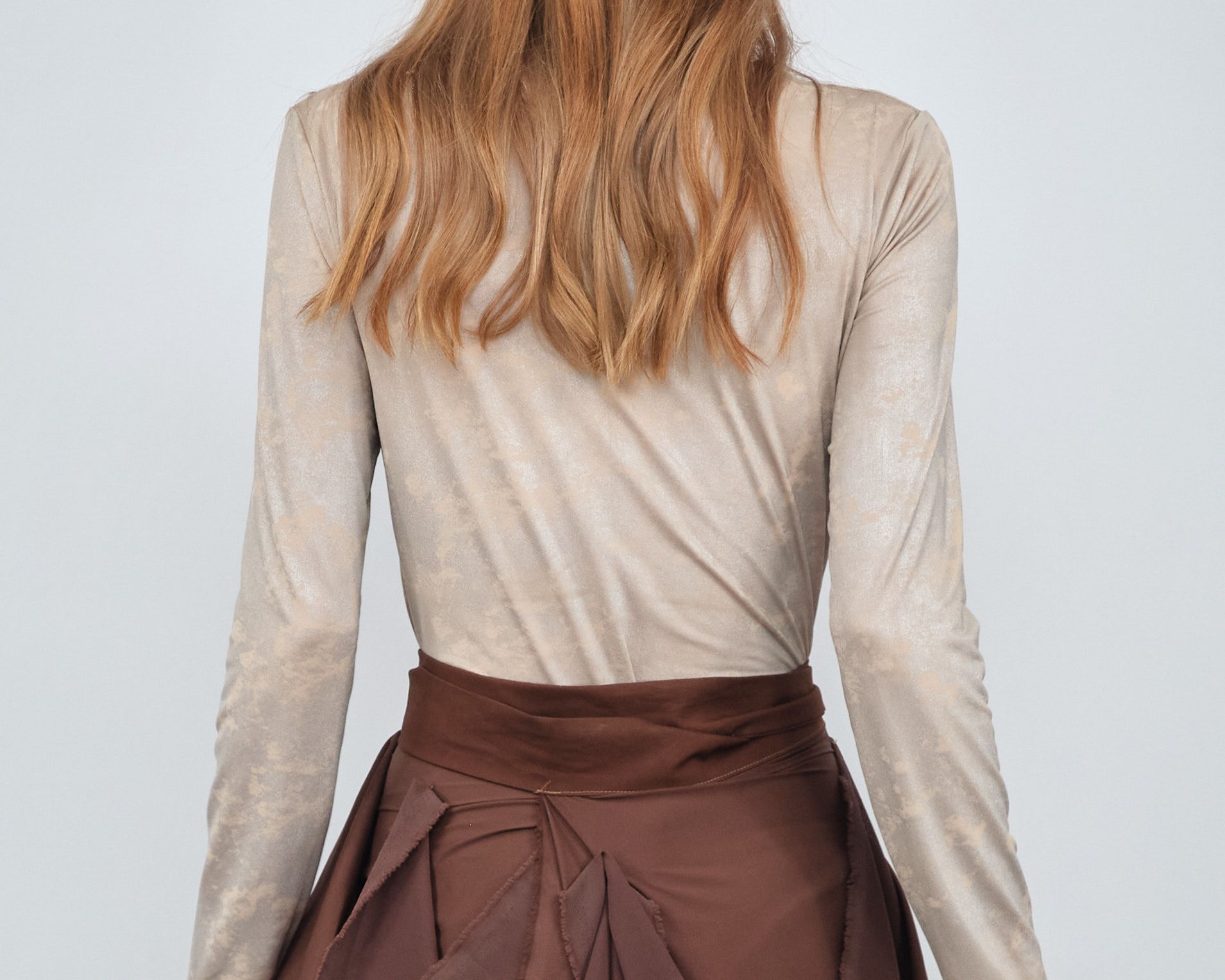 The back of a woman wearing a long sleeve top and a brown skirt