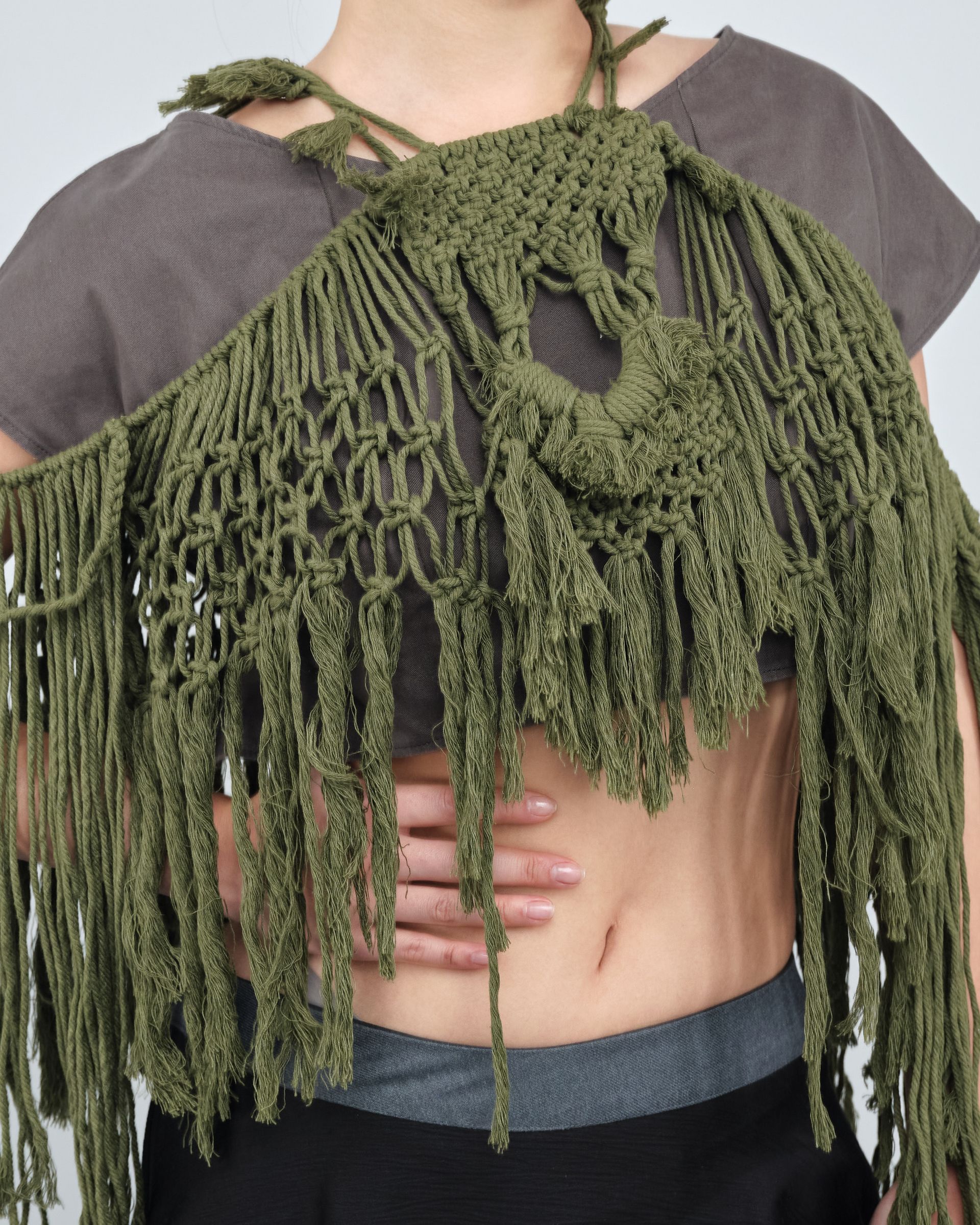 A woman is wearing a green crocheted top with fringe