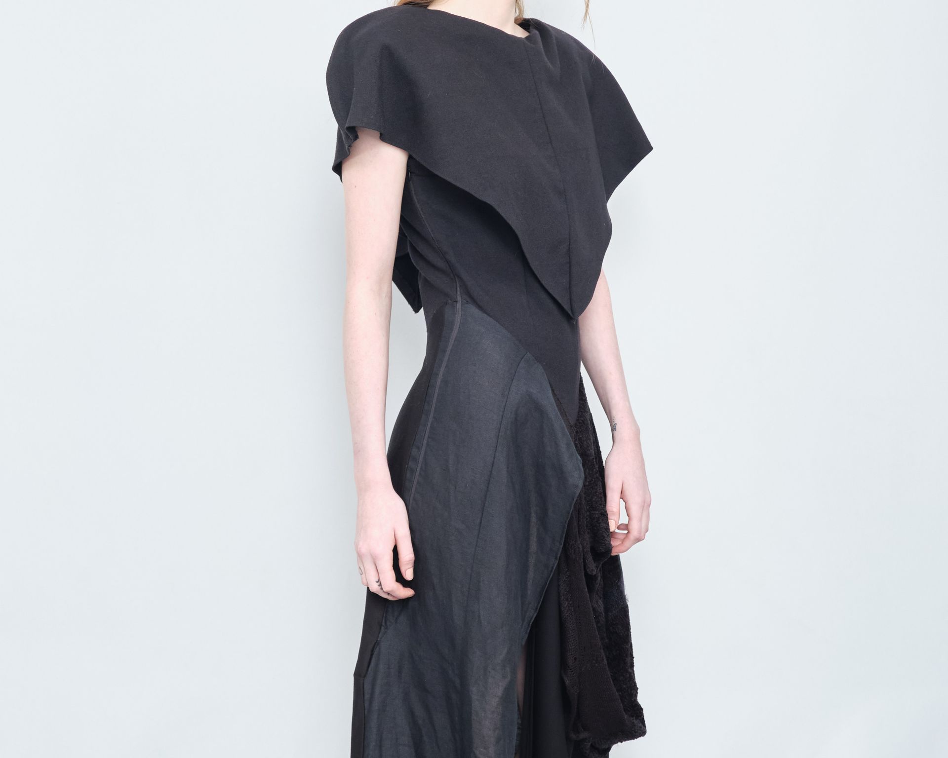 A woman in a black dress is standing in front of a white wall