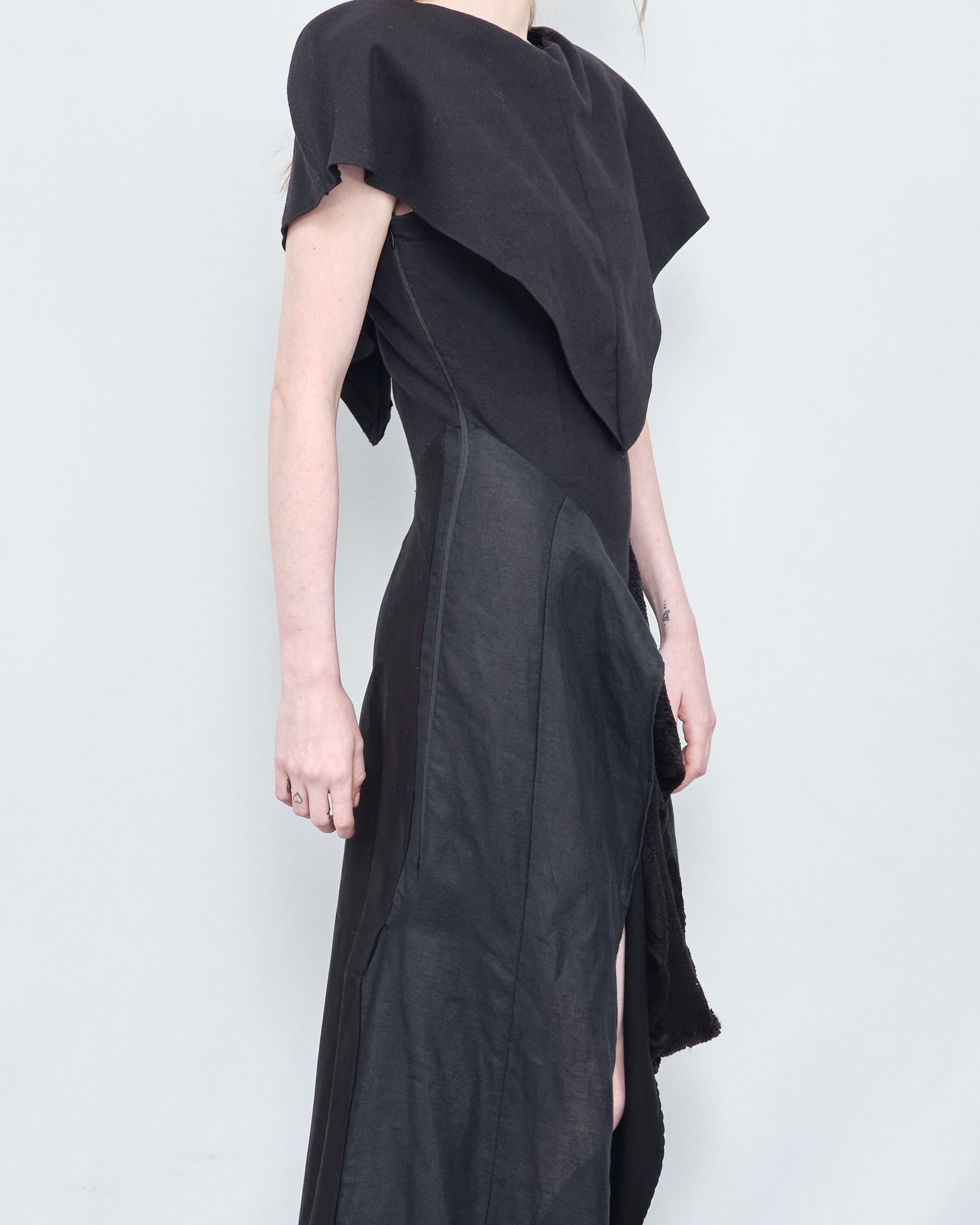 A woman in a black dress is standing in front of a white wall