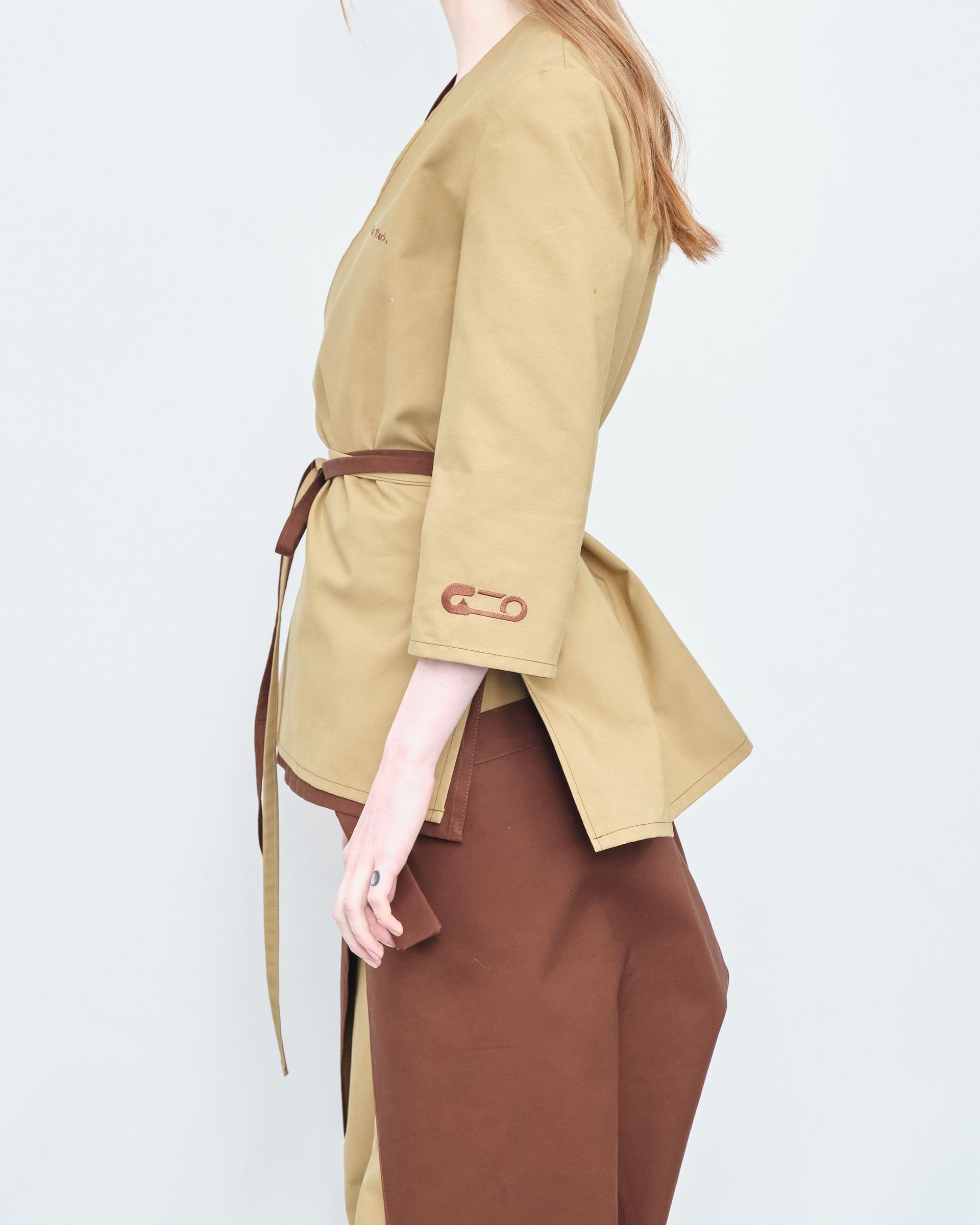 A woman is wearing a tan jacket and brown pants