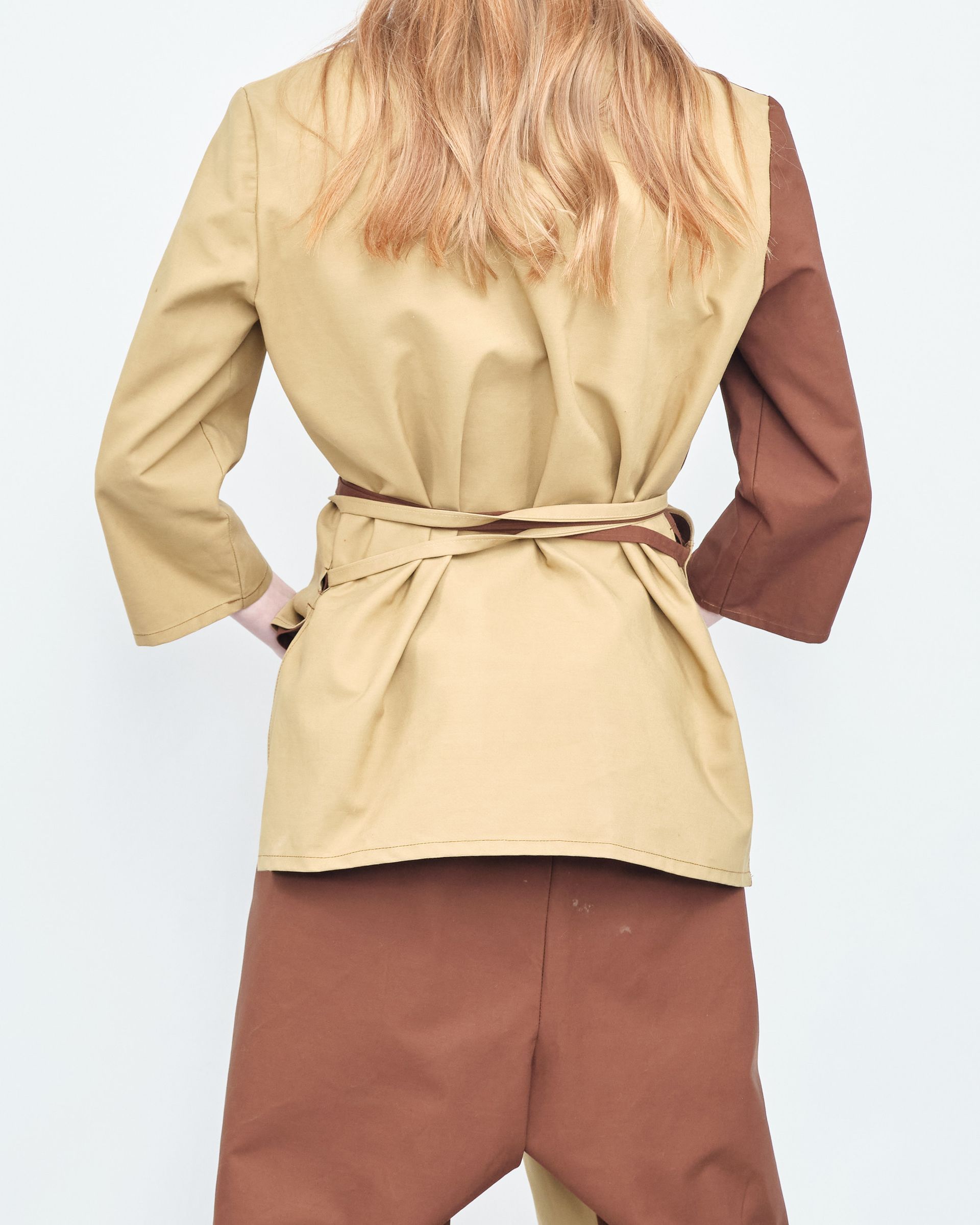 A woman is wearing a tan jacket and brown pants
