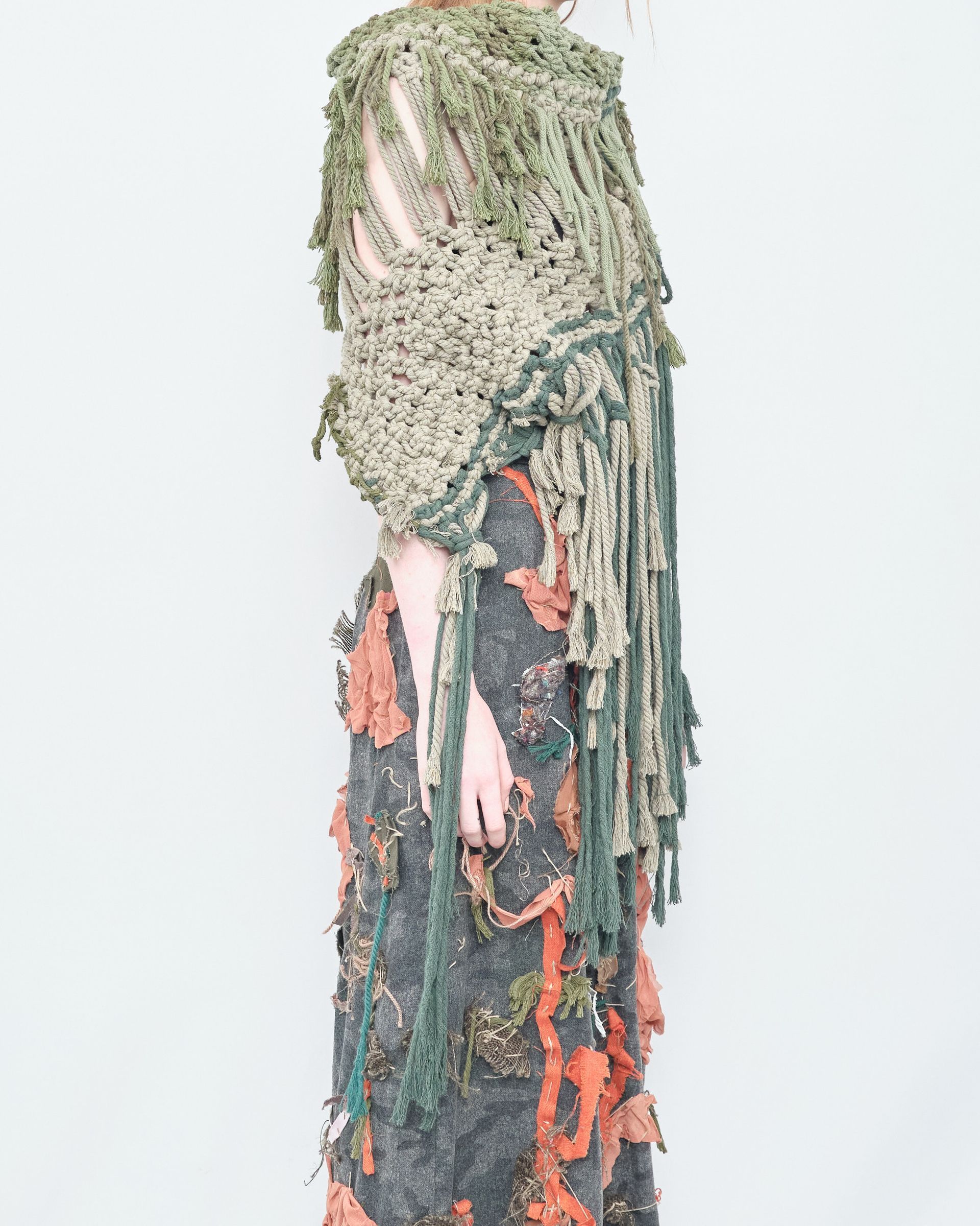 A woman is wearing a green crocheted shawl with fringe.
