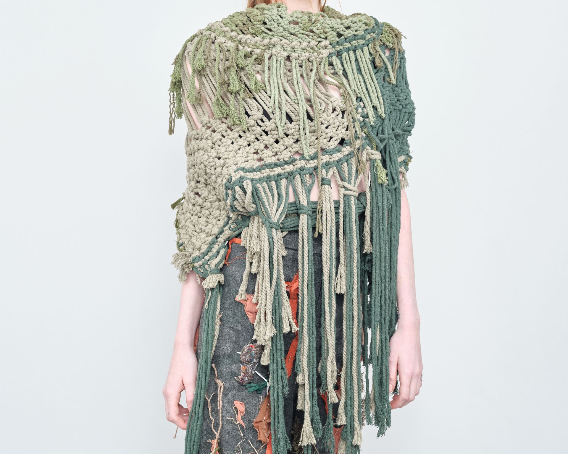 A woman is wearing a green crocheted shawl with fringe.