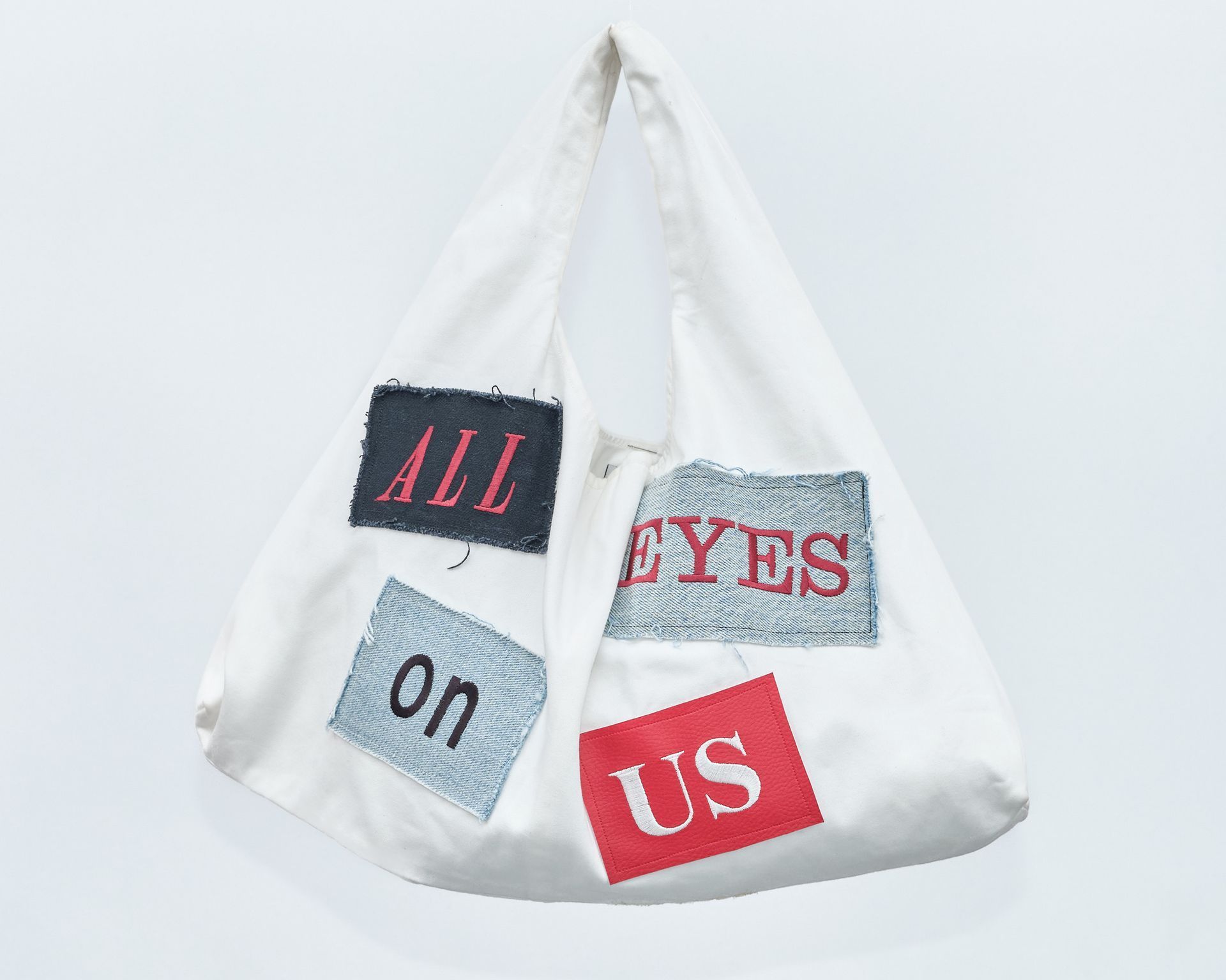 A white bag with the words `` all eyes on us '' embroidered on it.
