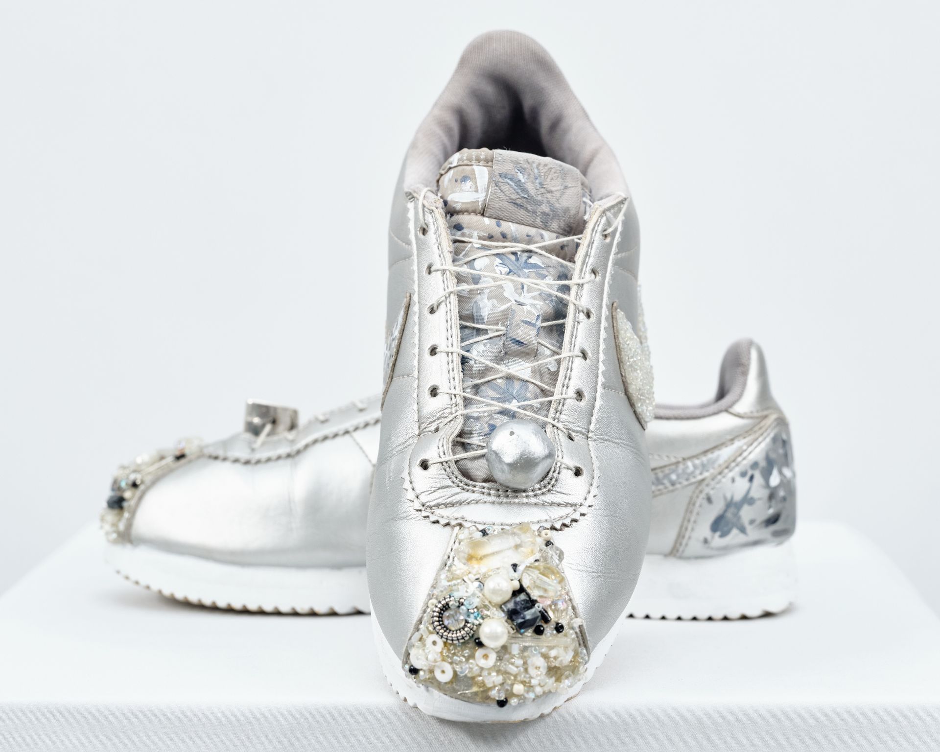 A pair of silver sneakers with pearls and rhinestones on them