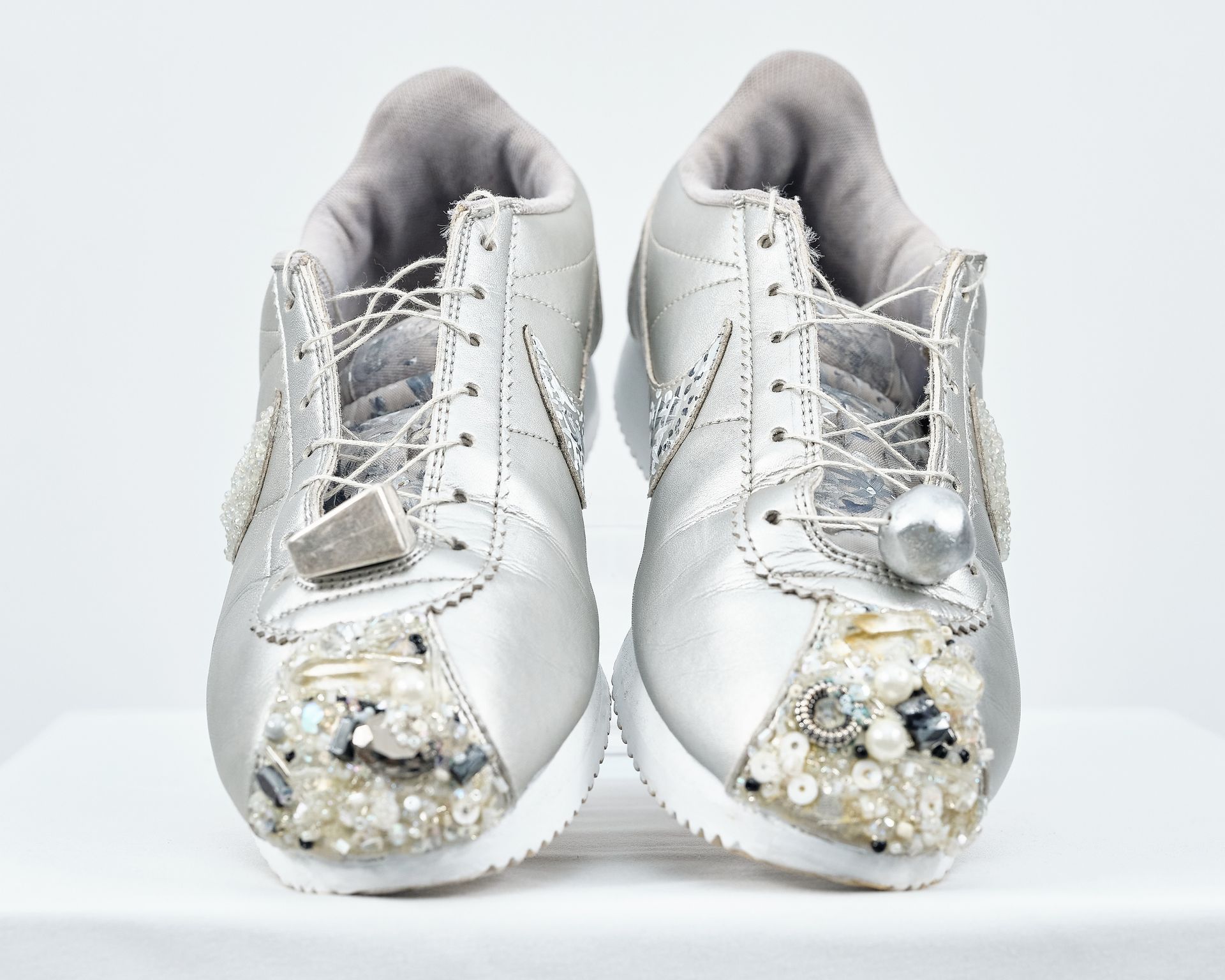 A pair of silver sneakers with pearls and rhinestones on them