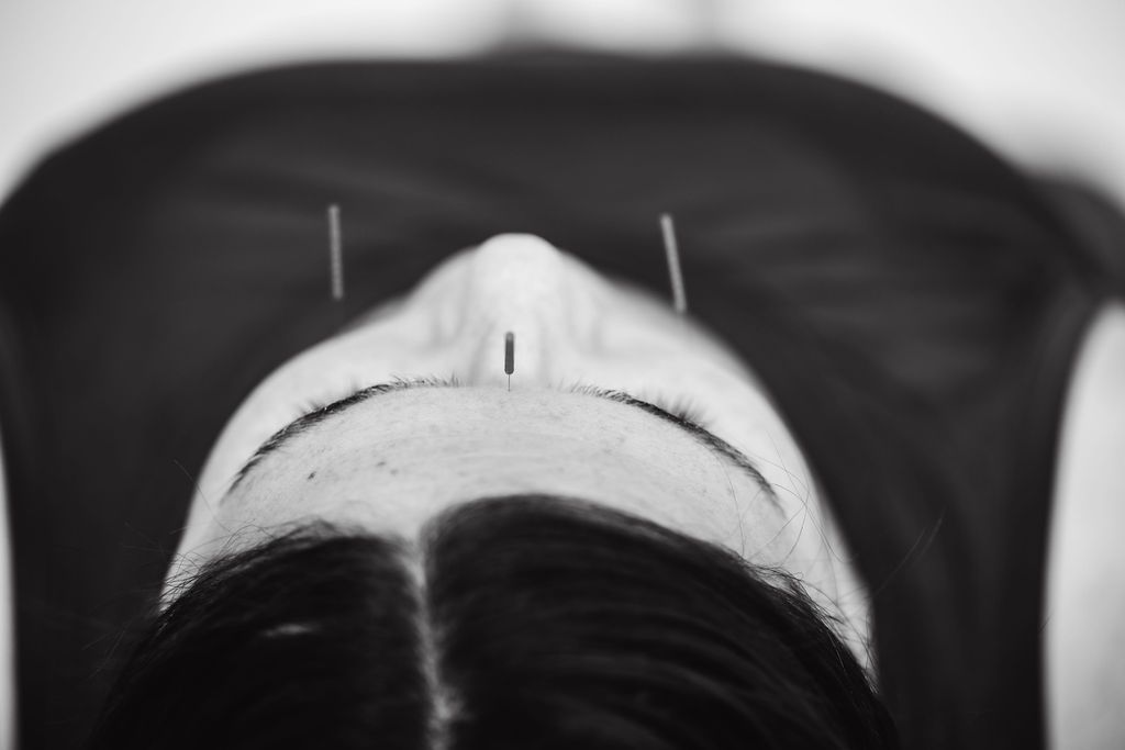 Overhead black-and-white portrait of a person lying back on a dark surface, face centered and partially in shadow