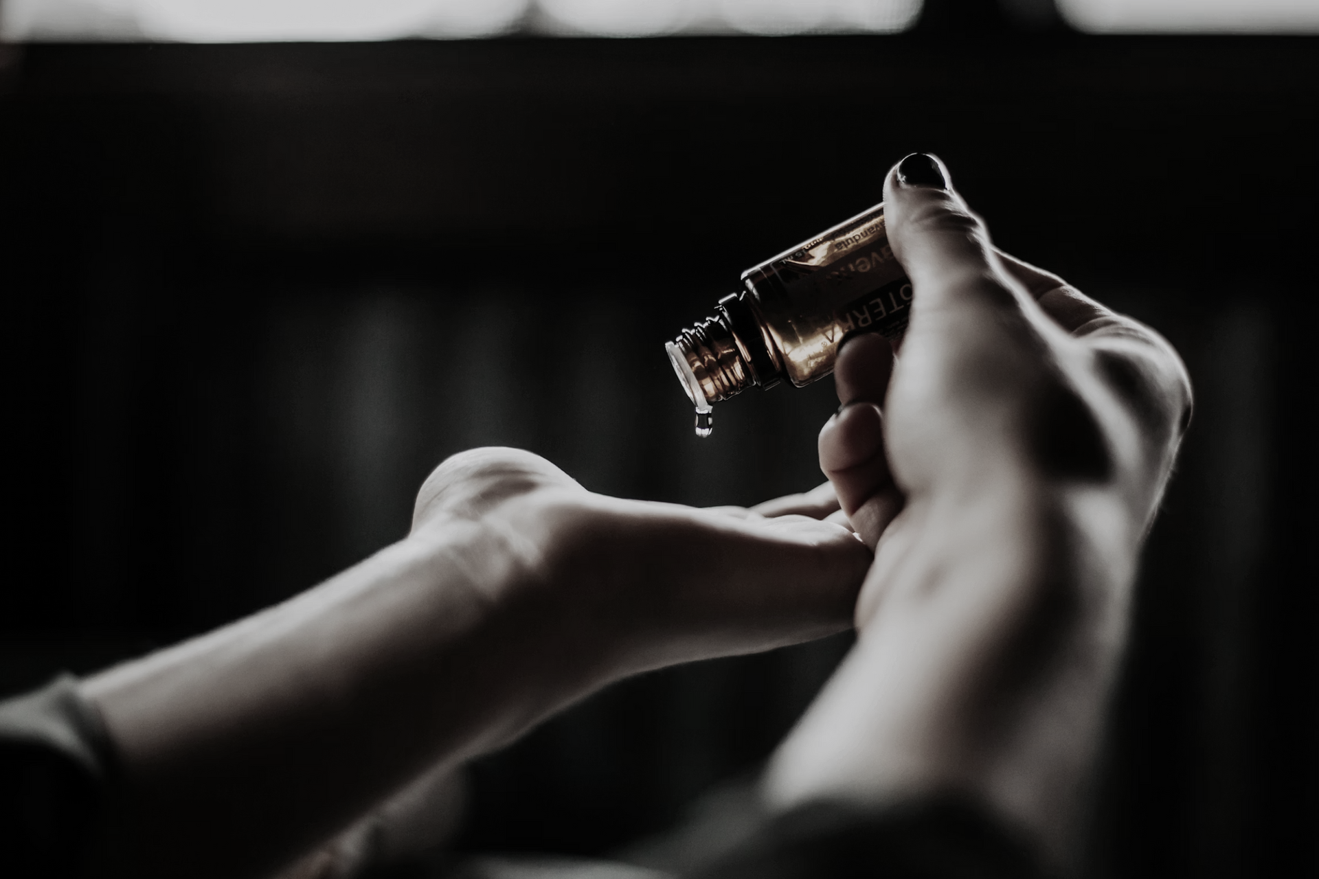 Hands holding a small amber glass bottle against a dark background