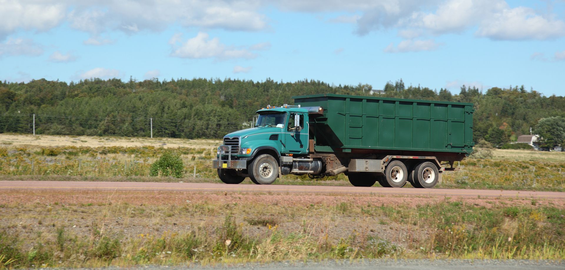 A green dump truck is driving down a dirt road