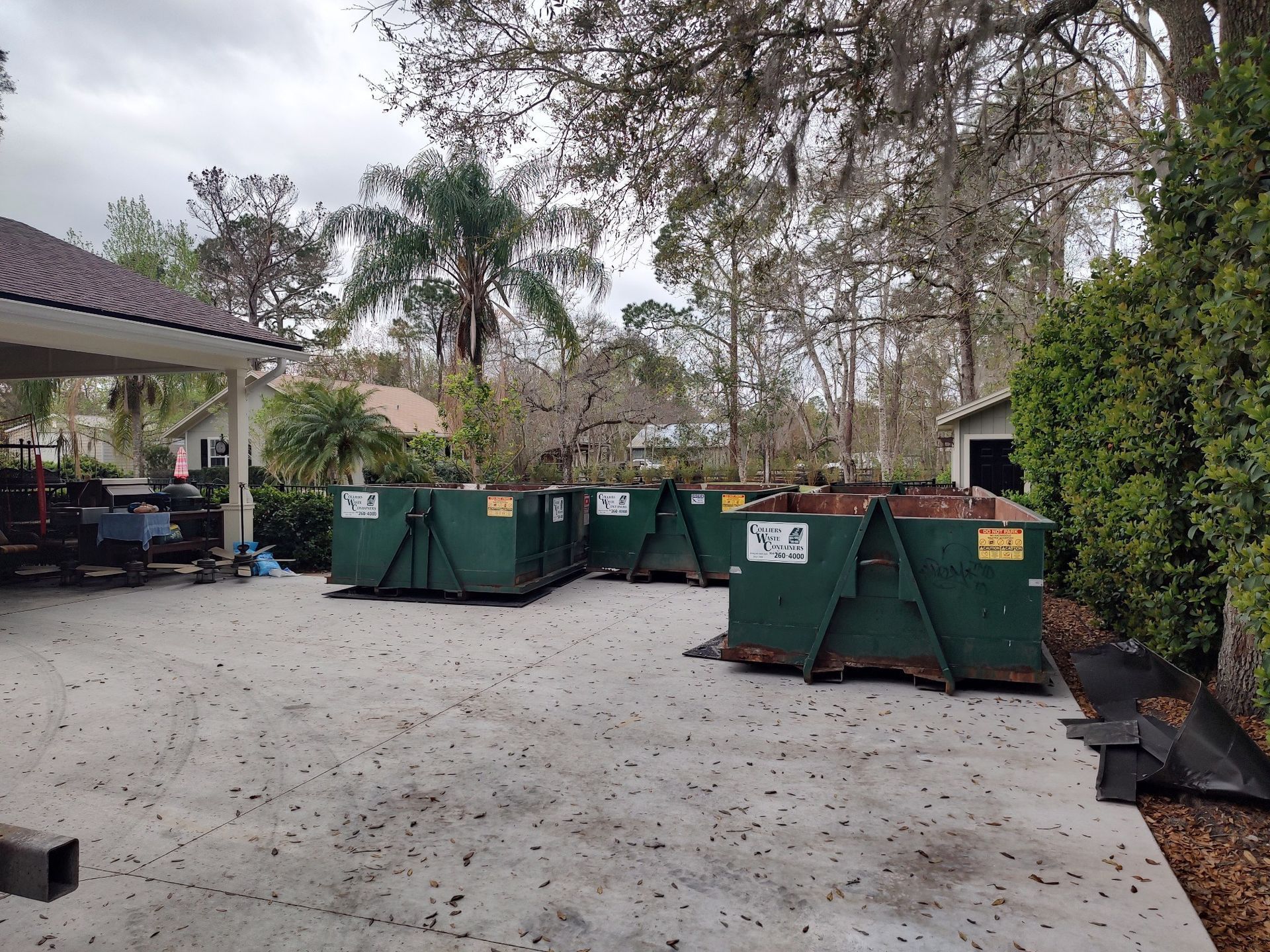 A row of dumpsters are parked in a driveway in front of a house.