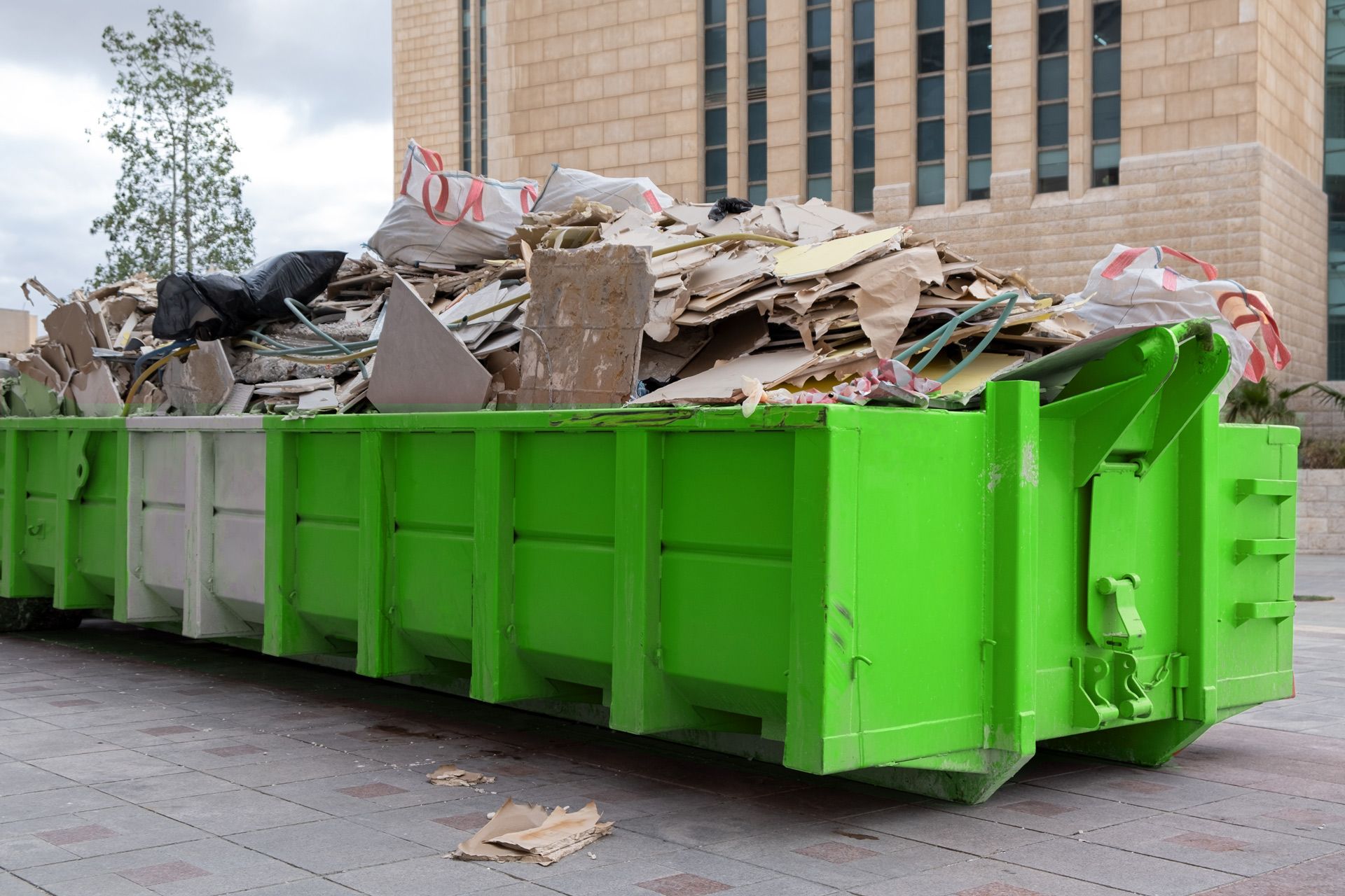 A green dumpster filled with cardboard is parked in front of a brick building.