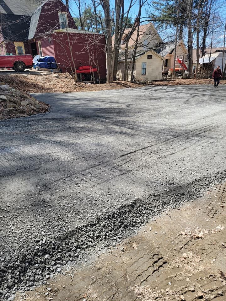 A newly spread gravel driveway leads toward a red house and a small yellow building in a residential neighborhood.