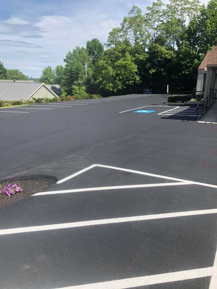 Newly paved black asphalt driveway in front of a blue-gray house with a white garage door, yellow markings, and a white sign.