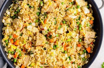 Chicken fried rice with peas, carrots, and onions in a black skillet.