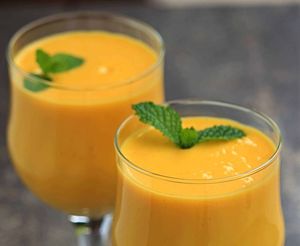 Two glasses of orange mango smoothie, garnished with mint sprigs, on a dark gray surface.