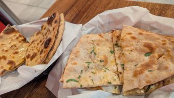 Two baskets of naan bread, one plain, one with herbs, on a wooden board.