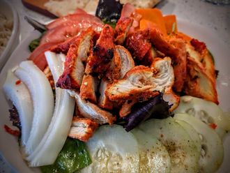 Grilled chicken salad with tomato, onion, cucumber, and orange slices.