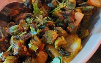 Close-up of a dish with fried okra, potatoes, and herbs in a white bowl.