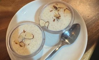 Two small bowls of rice pudding, topped with almond slivers, on a white plate with a spoon.