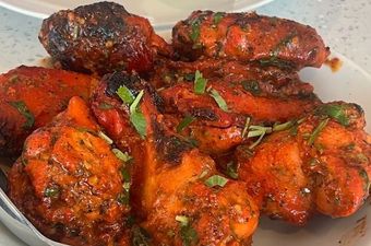 Close-up of grilled chicken tandoori, bright red with herbs.