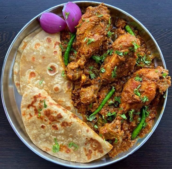 Chicken curry with roti and onion garnish on a steel plate.