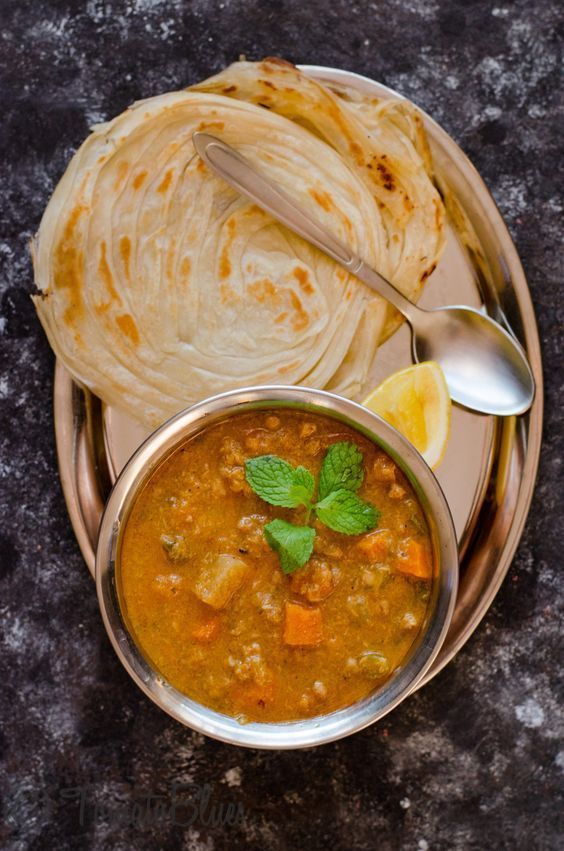 Bowl of stew with bread and lemon on a silver tray.