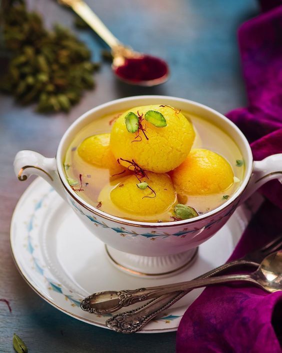 Rasmalai in a decorative cup, yellow sweet dumplings in a milky saffron-infused syrup.