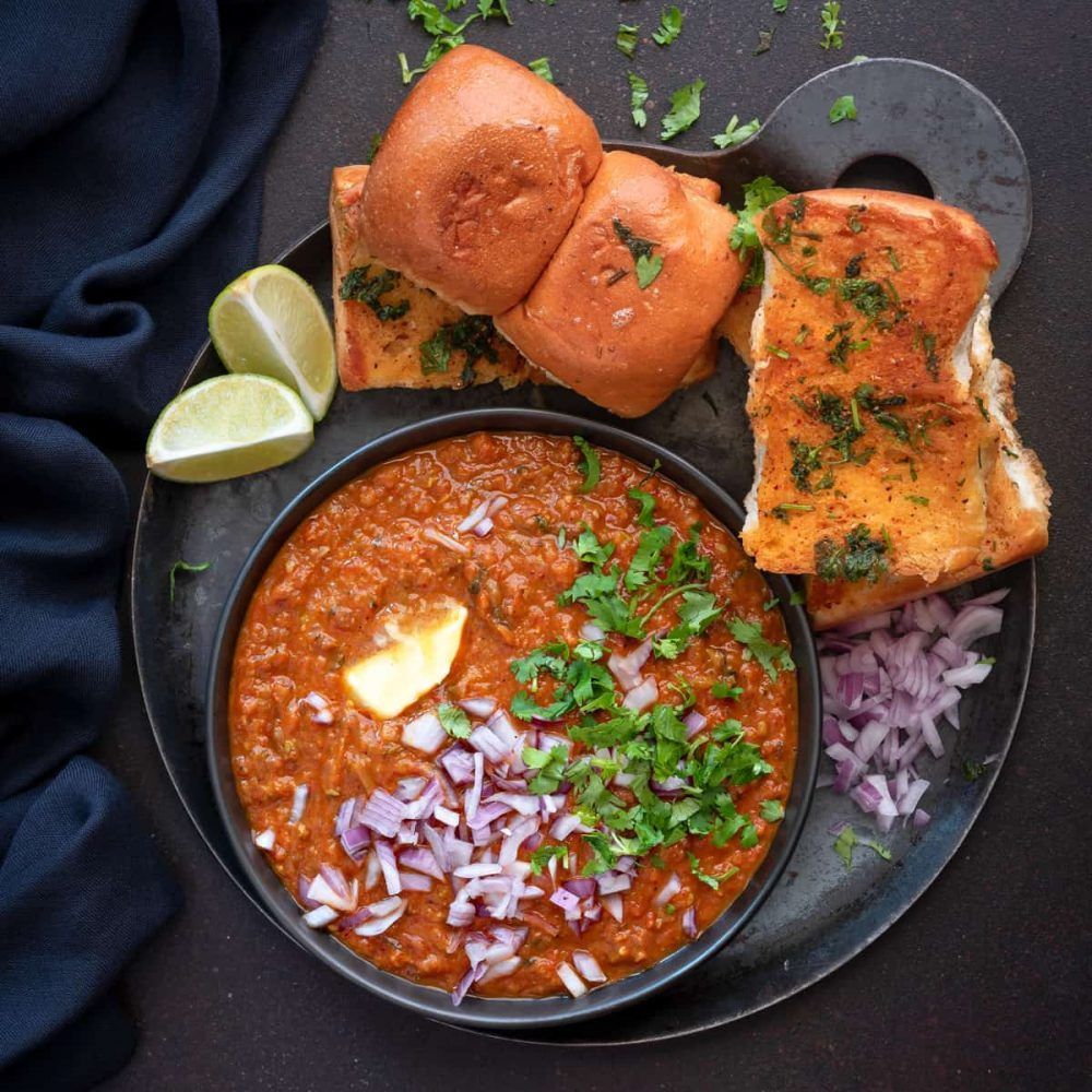 Pav bhaji: A bowl of spiced vegetable mash, served with buttered bread rolls, onions, lime, and coriander.