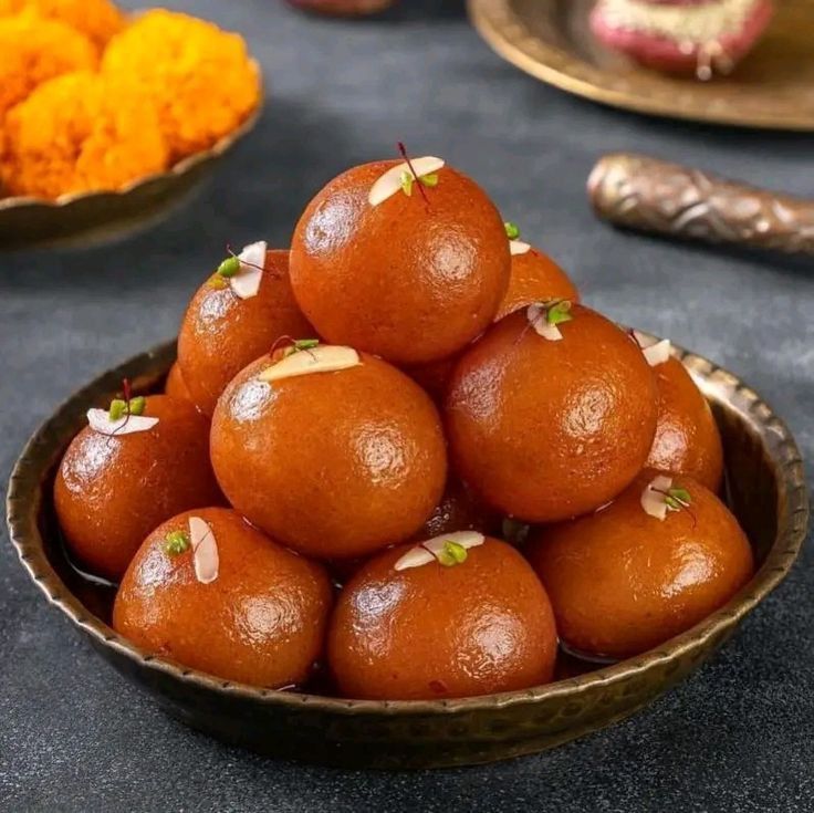 Bowl of golden brown gulab jamun, Indian dessert, garnished with nuts.